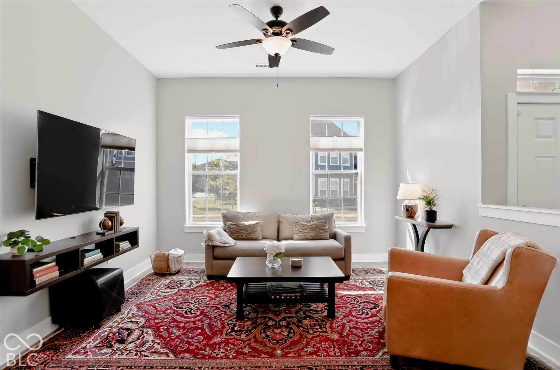 Living area featuring a ceiling fan with integrated lighting, a floating media console, and dual windows