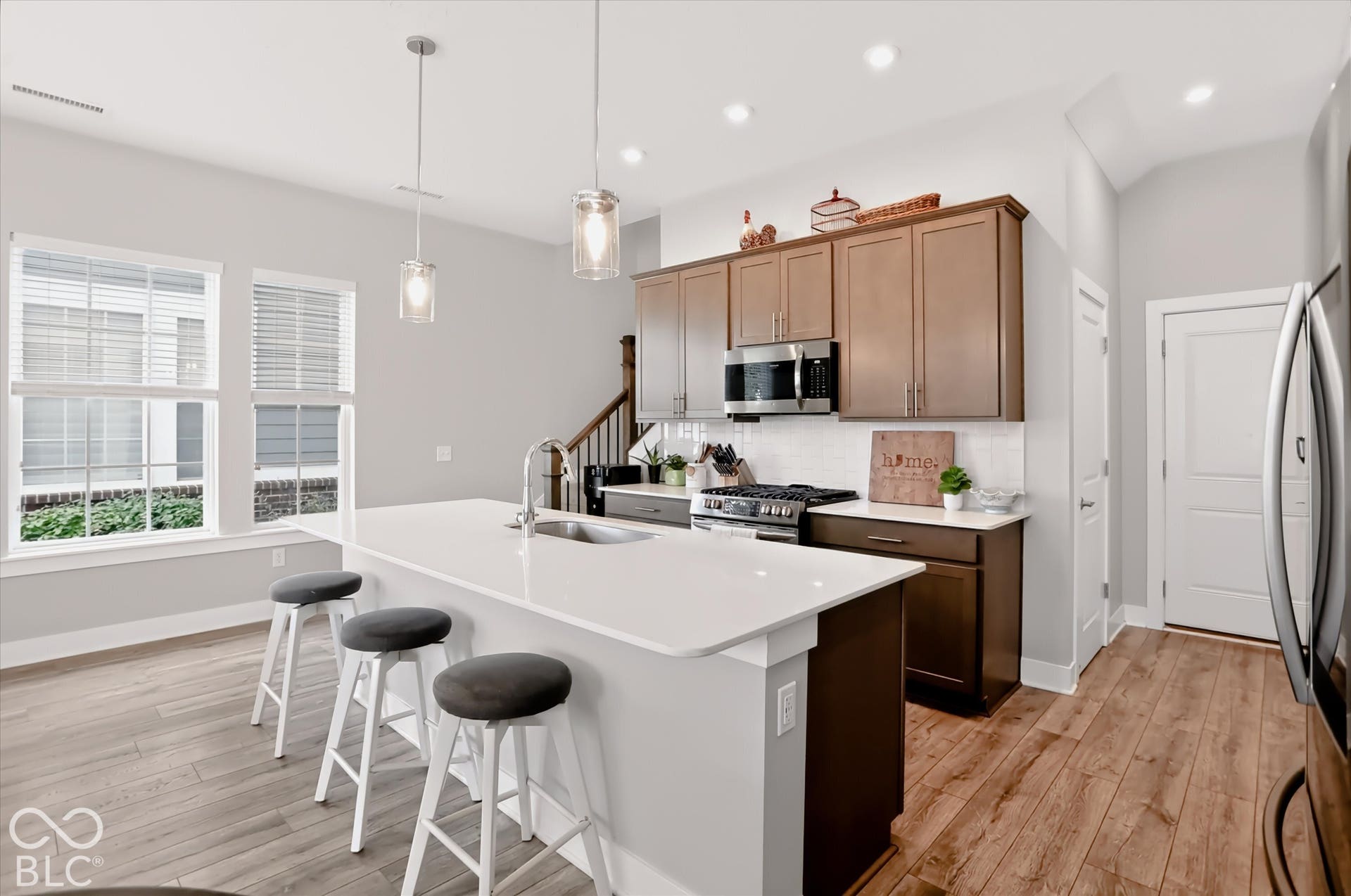 Kitchen featuring an island with built-in sink, stainless steel appliances, wood-finish flooring, and recessed lighting
