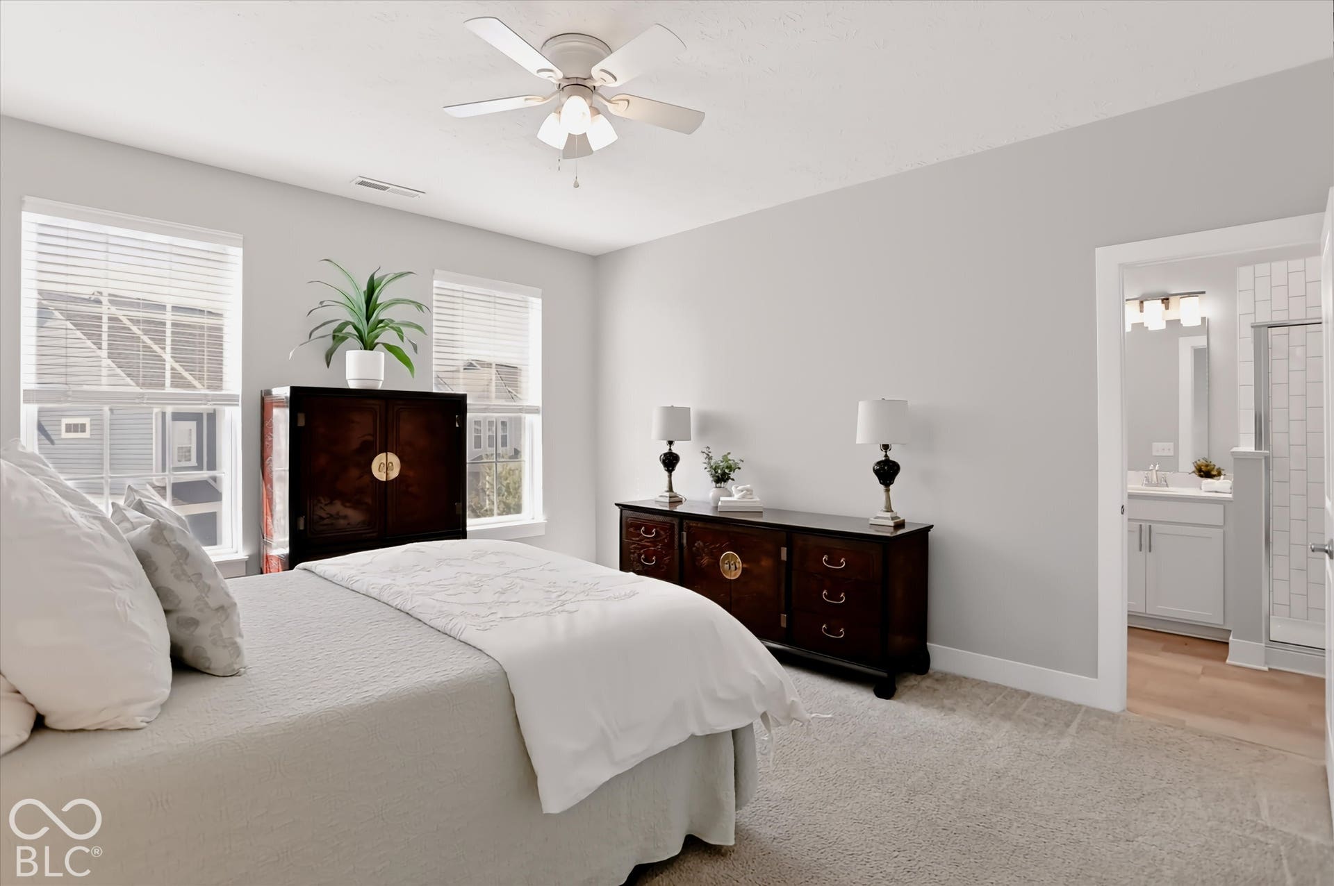 Carpeted room with a ceiling fan, two windows with blinds, and an open doorway revealing a bathroom with a vanity and shower enclosure