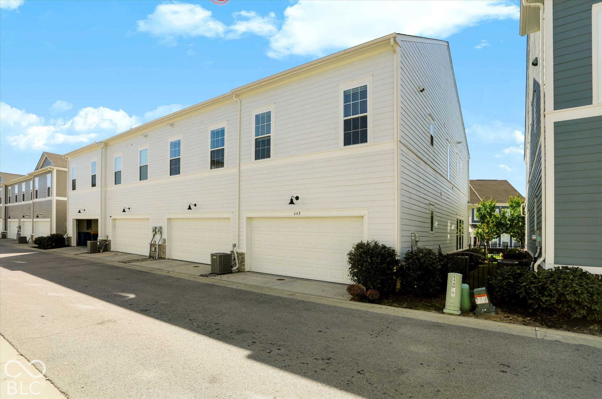 Light-colored siding exterior, multiple garage doors, and individual exterior lighting fixtures