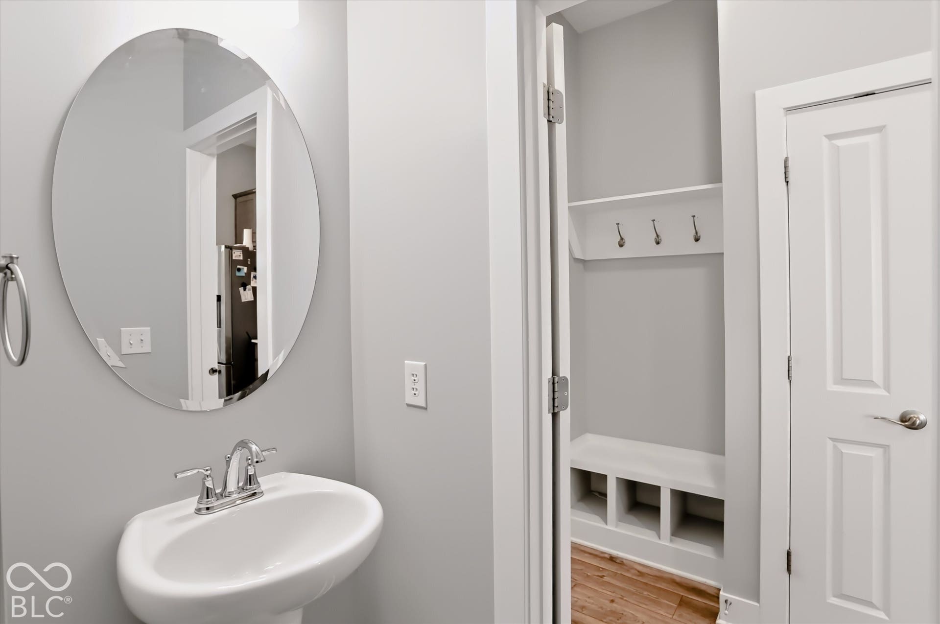 Pedestal sink with chrome faucet, oval frameless mirror, and built-in entry bench with storage cubbies and coat hooks