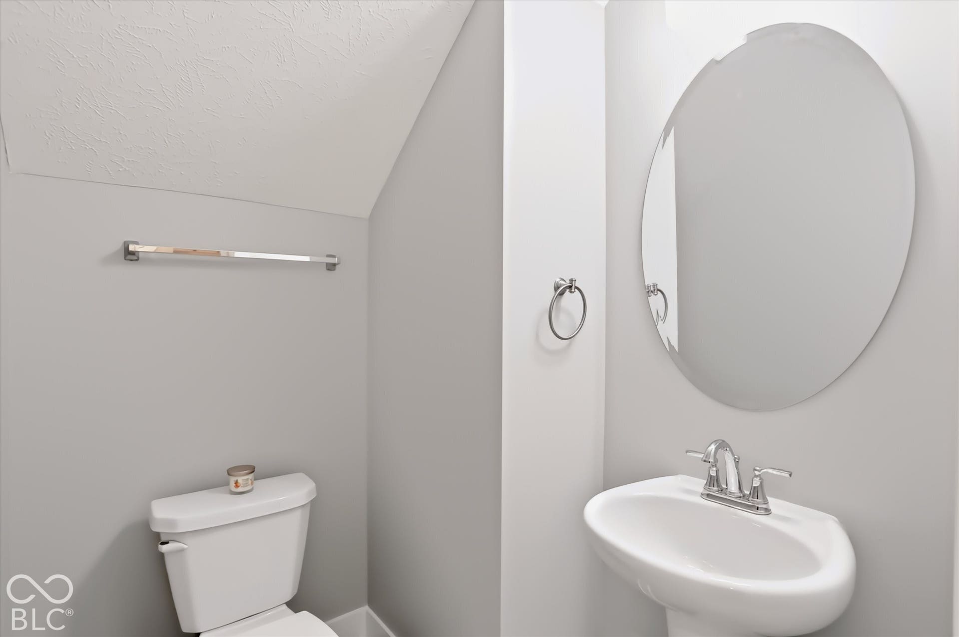 Pedestal sink with chrome fixtures, oval mirror, and a white toilet
