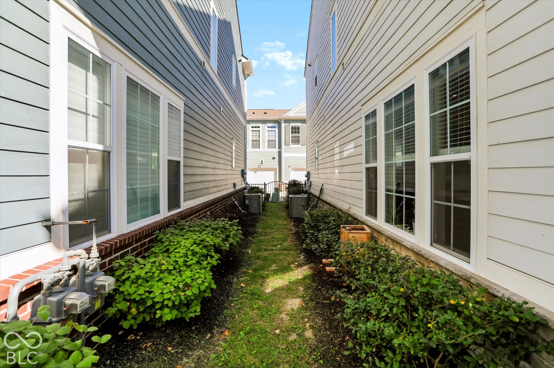 Siding exterior with multiple windows, brick foundation detail, and established landscaping.  Gated, shared lawn area.