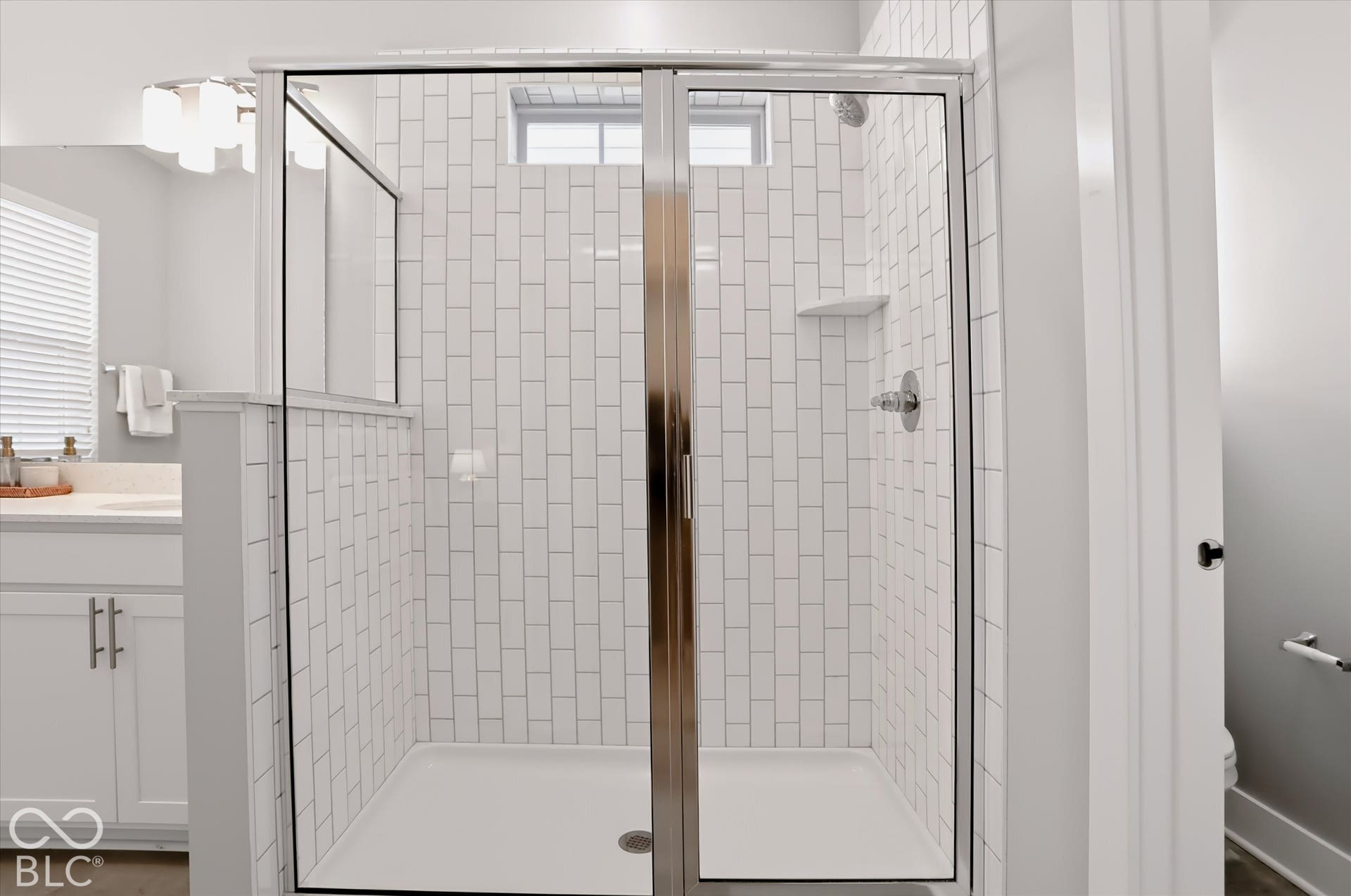 Glass-enclosed shower with subway tile surround, built-in shelving, and polished chrome fixtures