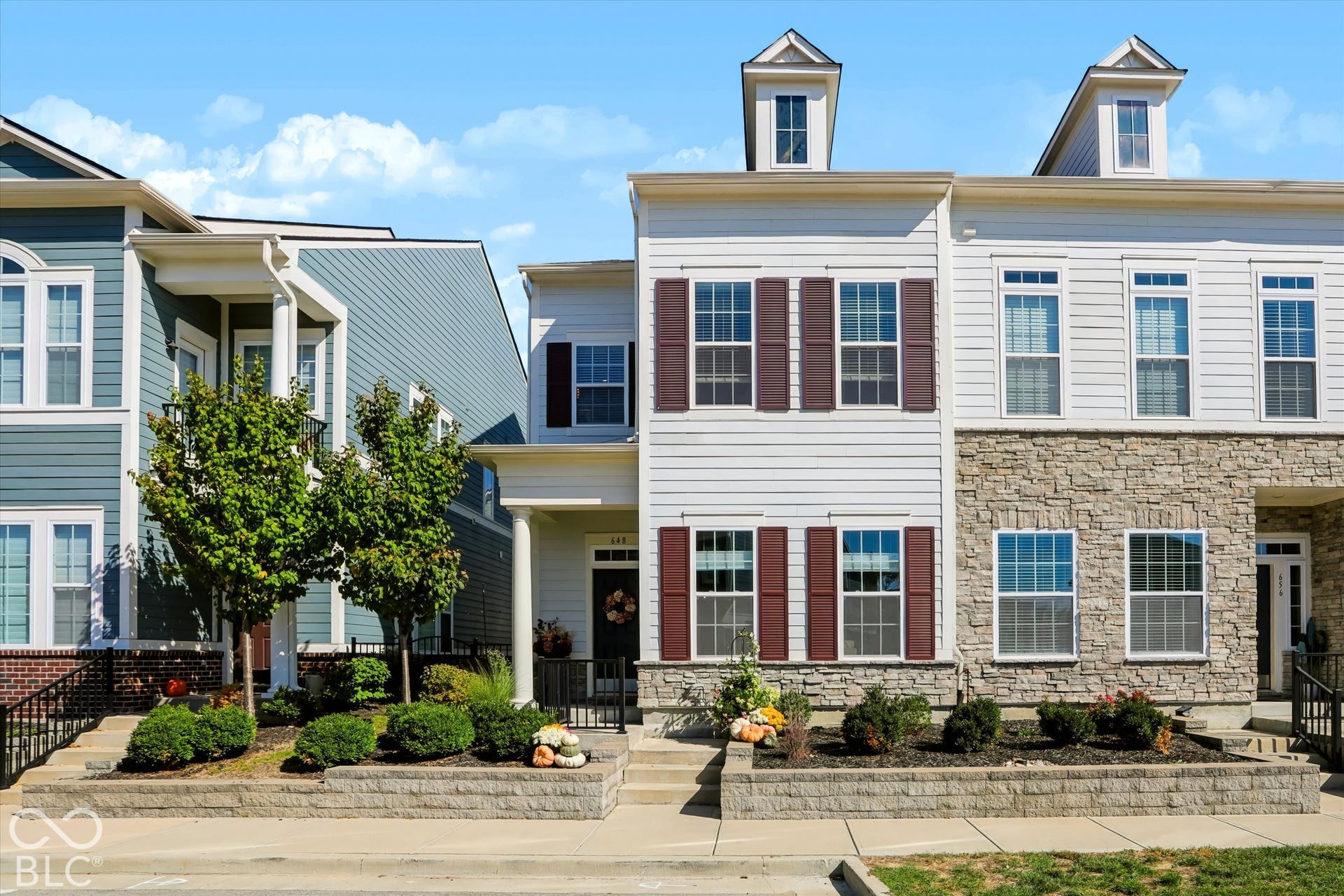 Multi-level townhome featuring a stone facade, white siding, and prominent dormer windows
