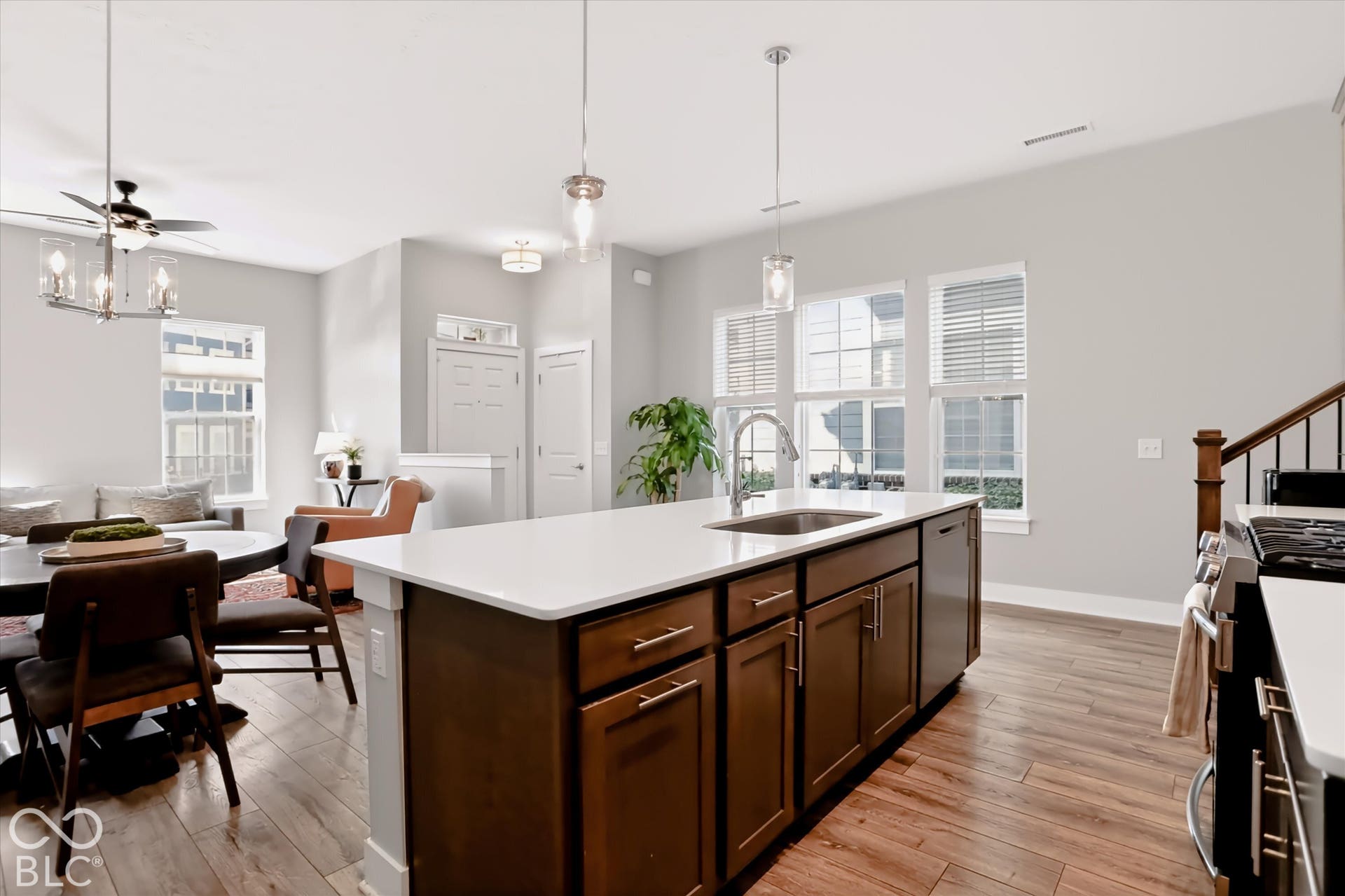 Kitchen island with a white countertop and dark wood-finish cabinetry, stainless steel sink with a gooseneck faucet, wood-finish flooring, and multiple windows with blinds