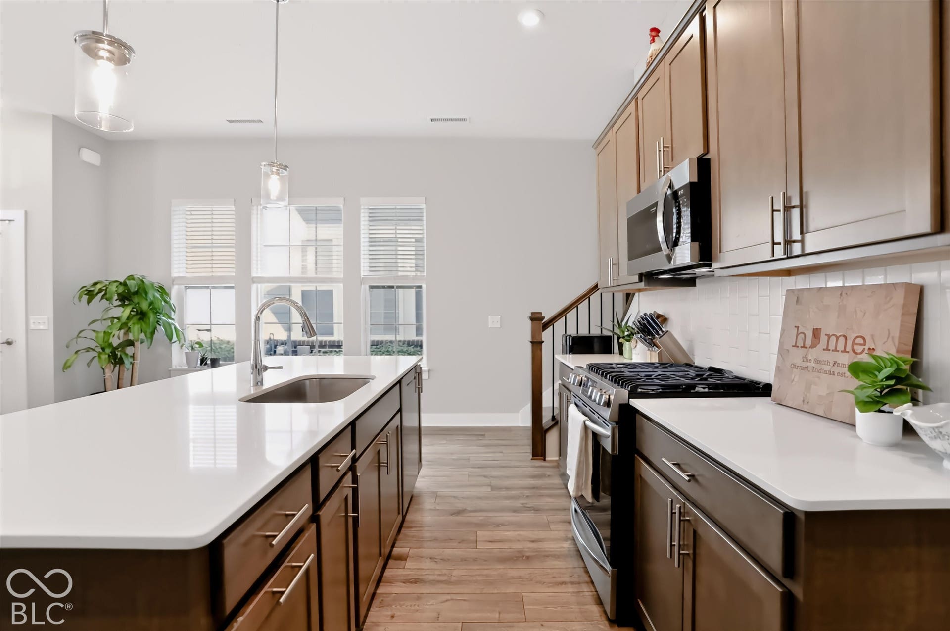 Kitchen featuring a large center island with an undermount sink, stainless steel appliances, a tile backsplash, and wood-finish flooring