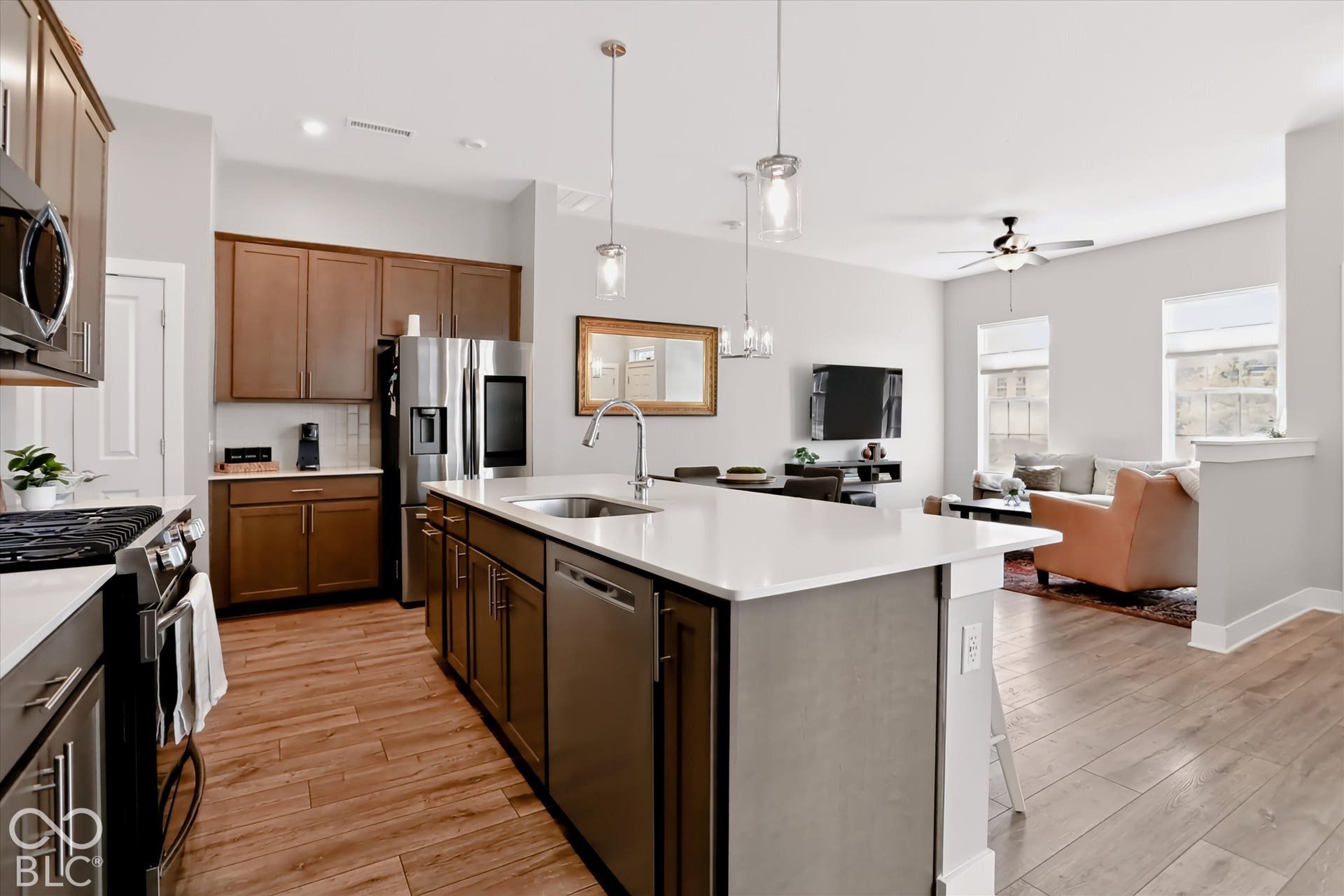 Kitchen island with white countertop and integrated sink, stainless steel appliances, wood-finish flooring, brown cabinetry, and pendant lighting