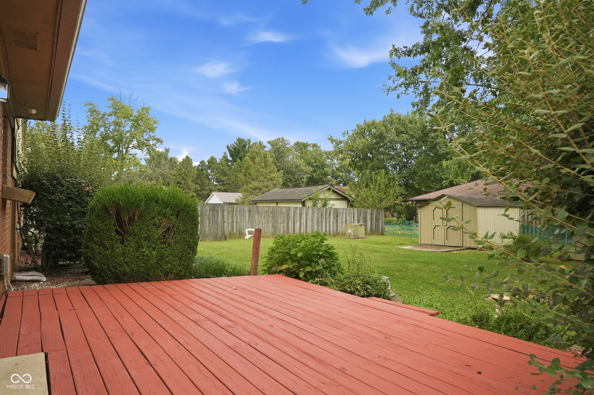 7927 Hoop Road, Indianapolis, IN 46217 Expansive wood deck with a red finish, large grassy yard, mature landscaping, and a storage shed