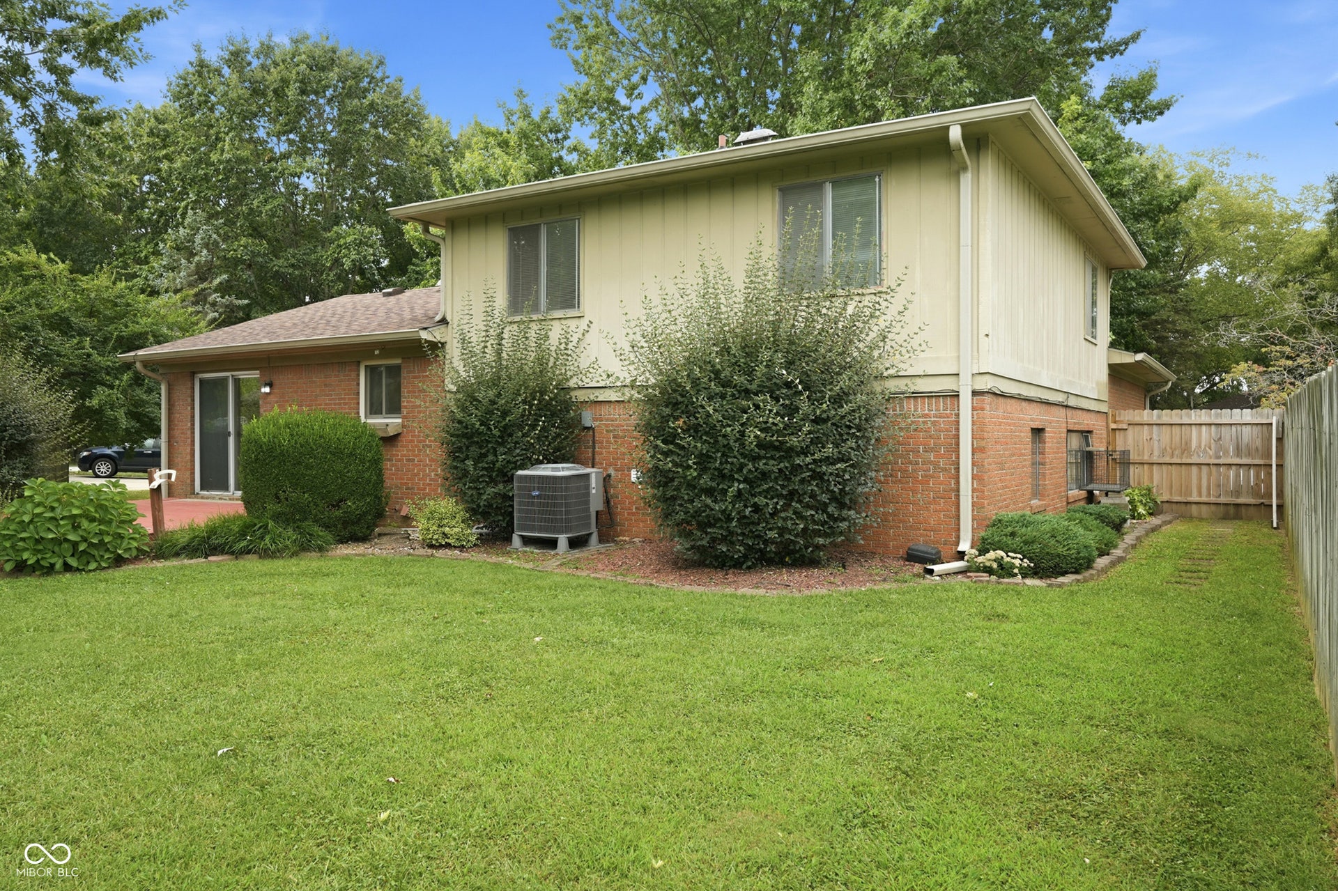 7927 Hoop Road, Indianapolis, IN 46217 Expansive lawn area, brick exterior, sliding glass door access, mature landscaping, and wood privacy fencing
