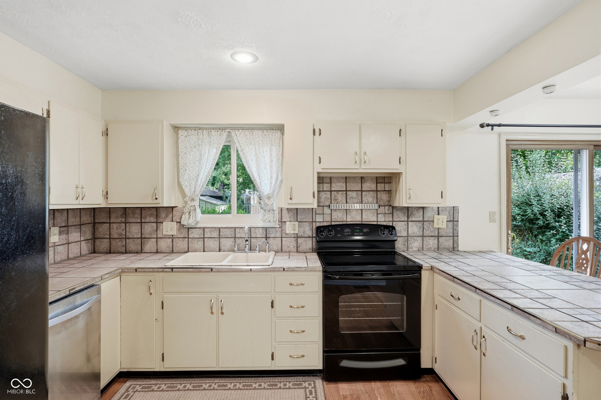 7927 Hoop Road, Indianapolis, IN 46217 Kitchen featuring tile countertops, white cabinetry, a double basin sink, and a black range