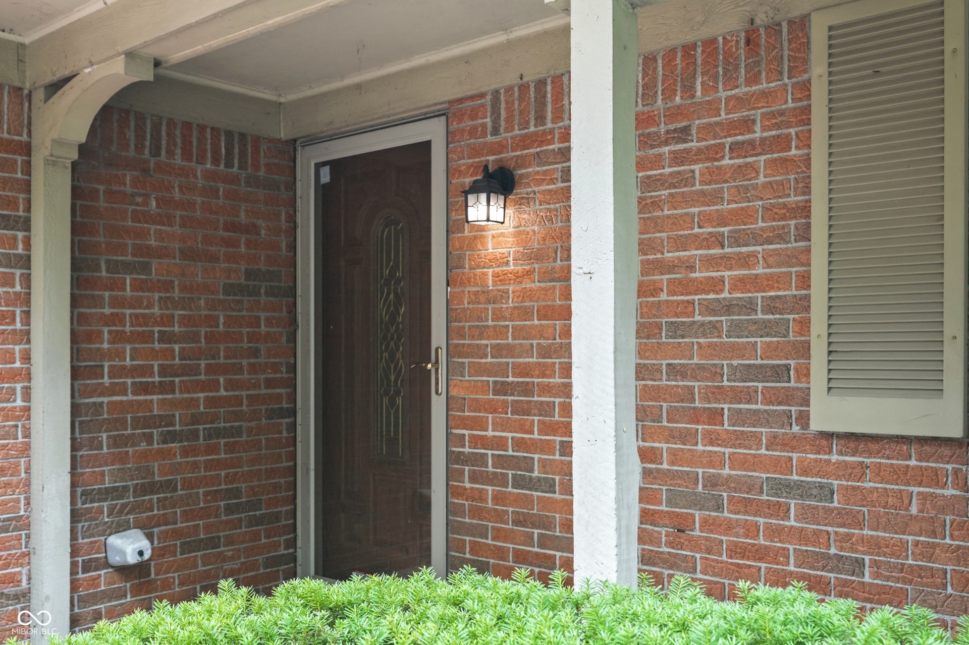 7927 Hoop Road, Indianapolis, IN 46217 Red brick exterior with a decorative wooden entry door, accented by a wall-mounted exterior light fixture and a louvered window shutter