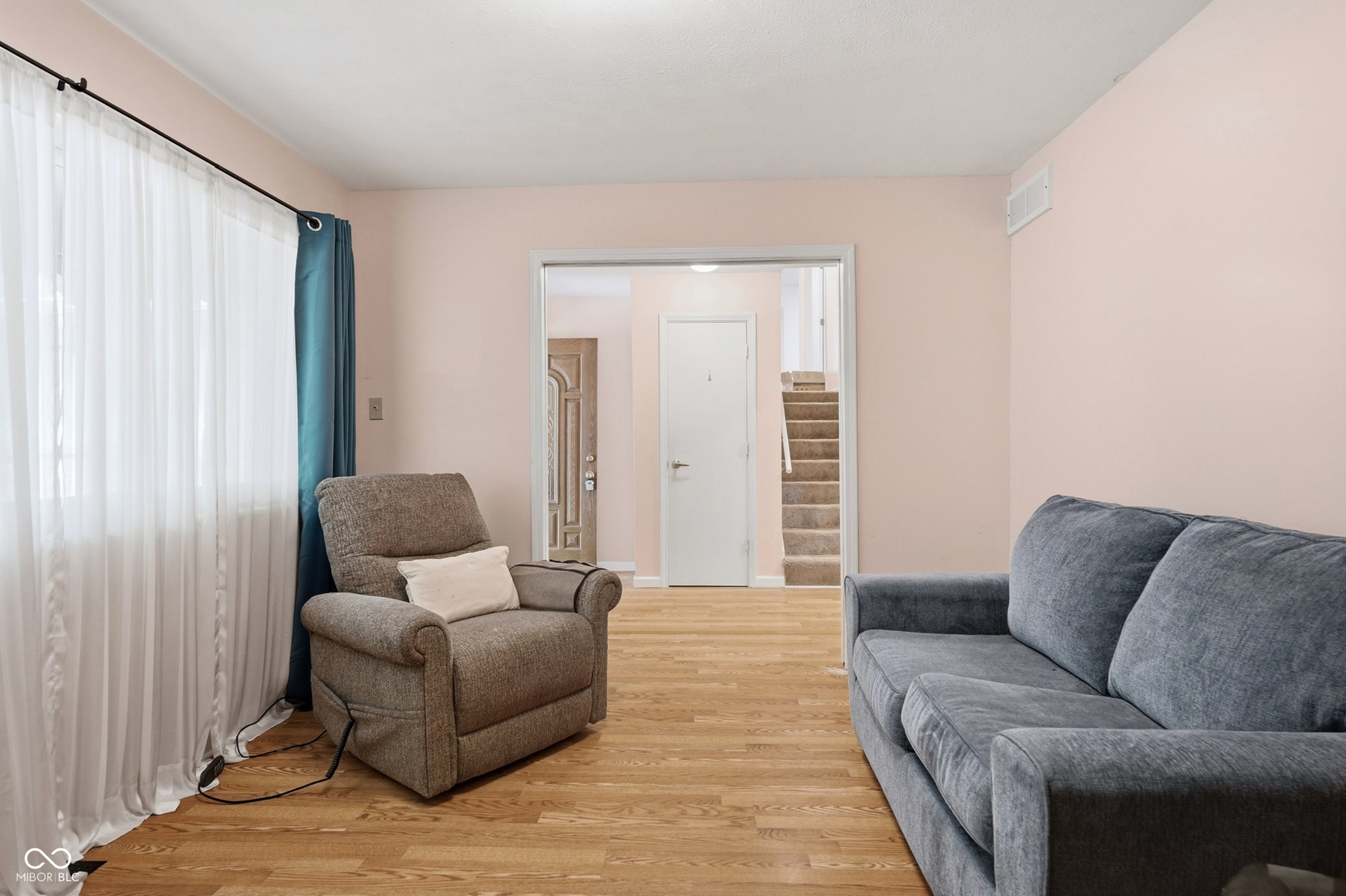 7927 Hoop Road, Indianapolis, IN 46217 Wood-finish laminate flooring, large picture window, light-toned wall paint, and an open doorway leading to a carpeted staircase