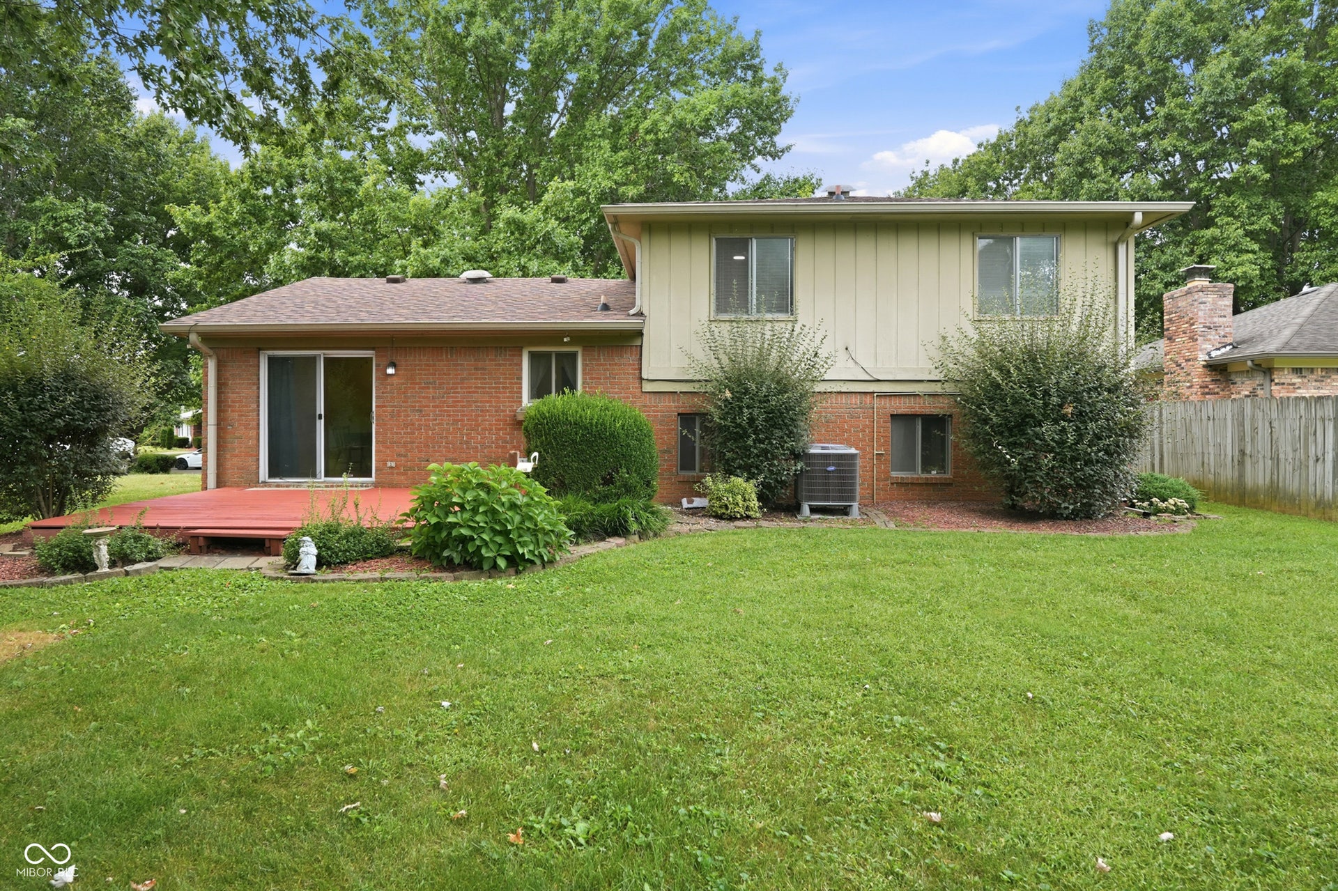 7927 Hoop Road, Indianapolis, IN 46217 Expansive lawn with a red-stained deck, brick and siding exterior, established shrubbery, and mature trees