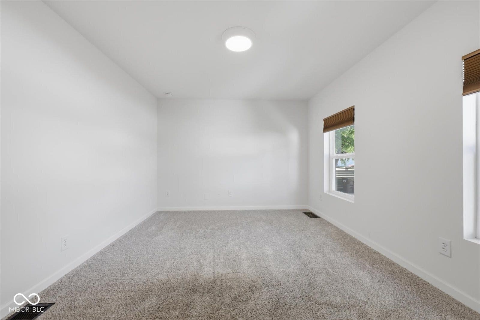 Light gray carpet flooring, white painted walls, and two windows with wood-finish blinds