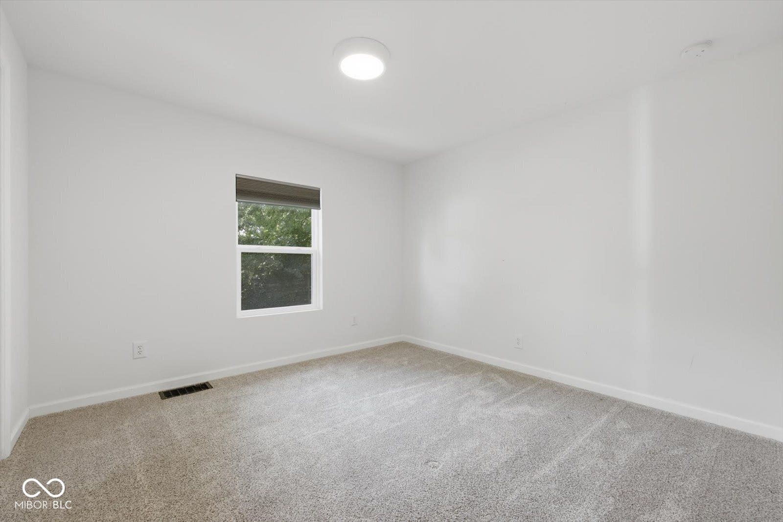 Neutral wall paint and carpeting, recessed lighting, and a single window with a roller shade