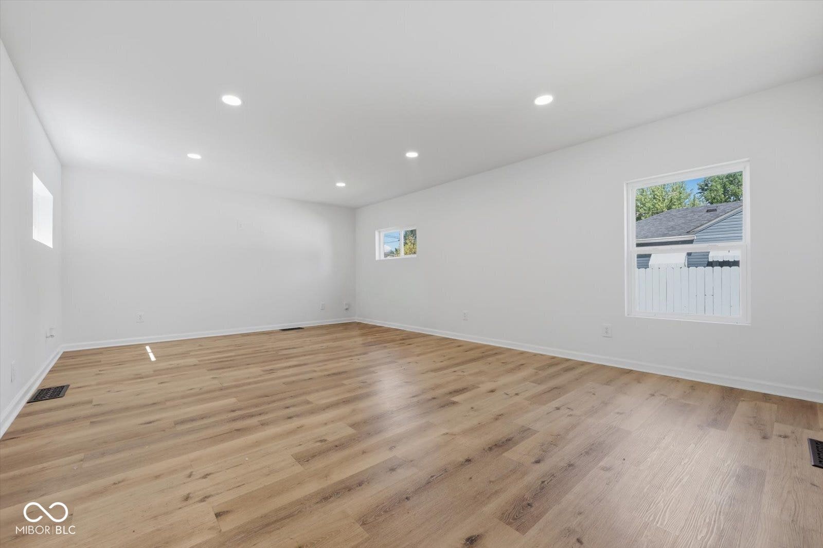 Spacious room with light wood-finish flooring, recessed lighting, white walls, and multiple windows