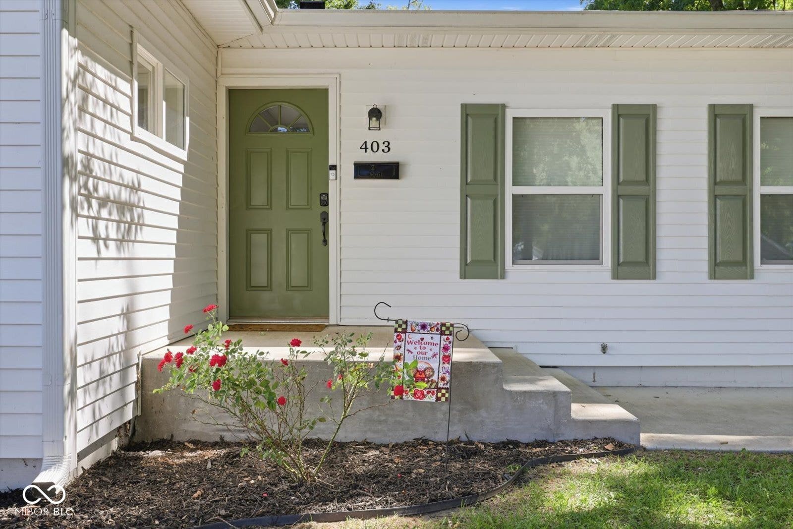 White siding exterior with a green paneled entry door, concrete steps, and decorative green shutters