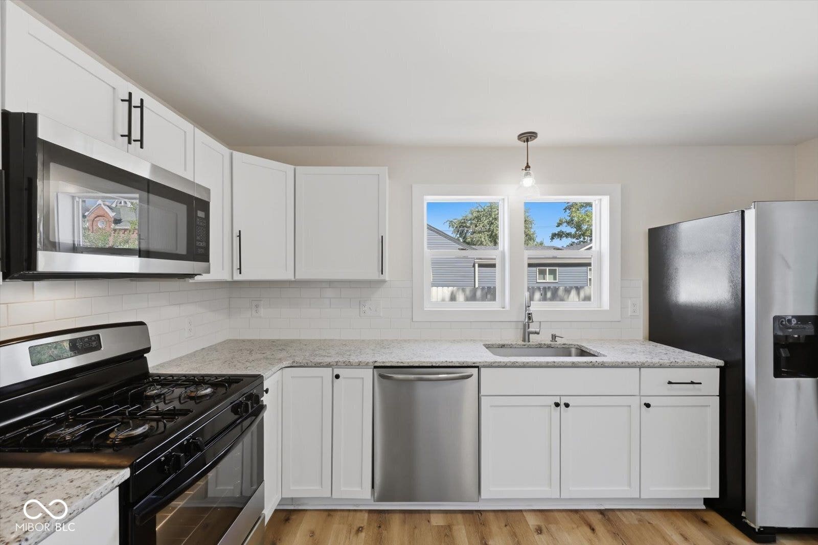 Contemporary kitchen featuring white cabinetry, stainless steel appliances, light-toned countertops, subway tile backsplash, and wood-finish flooring