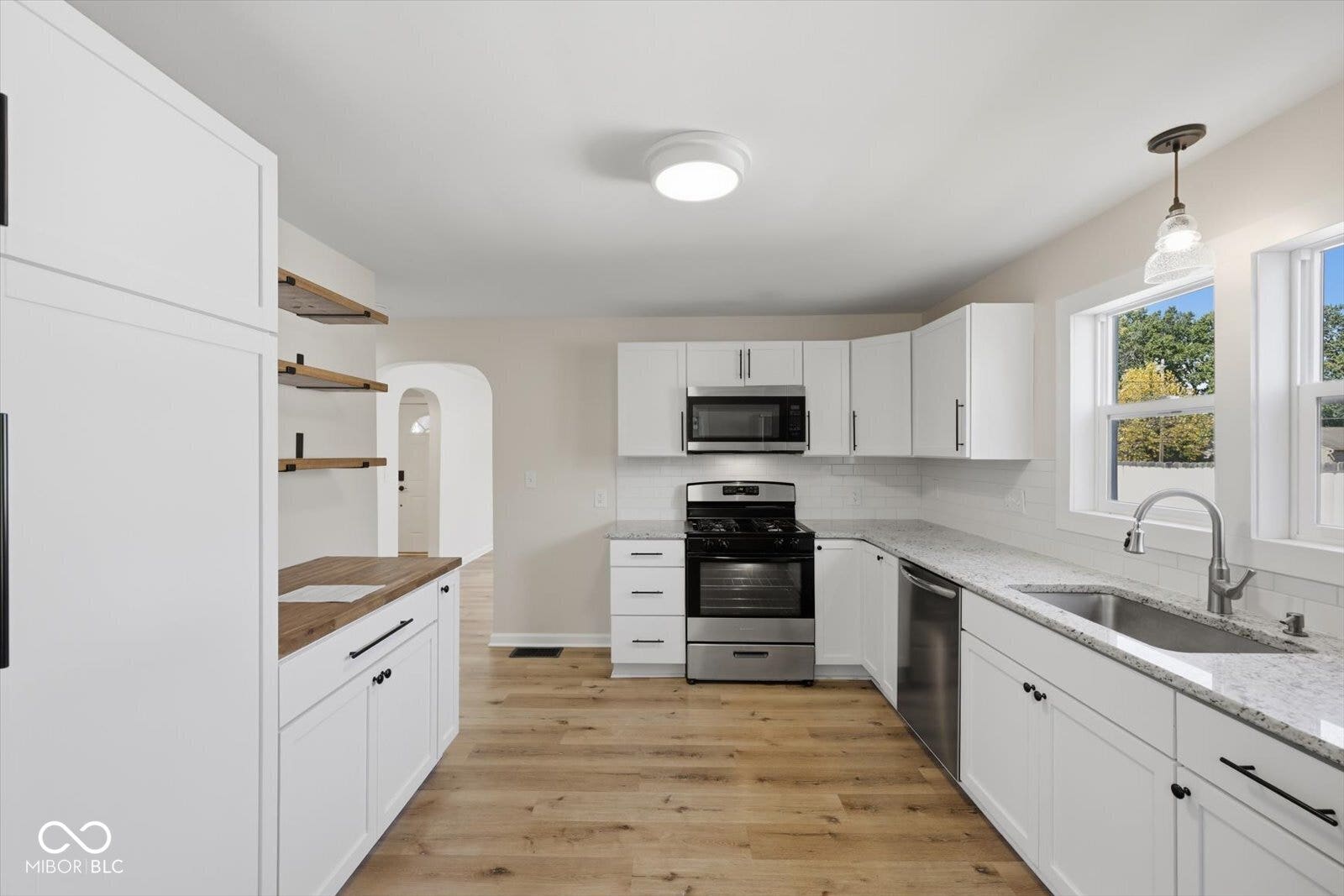 Modern kitchen featuring white cabinetry, stainless steel appliances, light-toned wood-finish flooring, and light-colored countertops