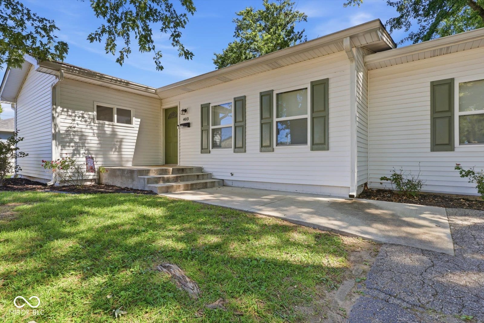 White siding exterior featuring multiple windows with green shutters, a green front door, and a concrete ramp leading to the entrance