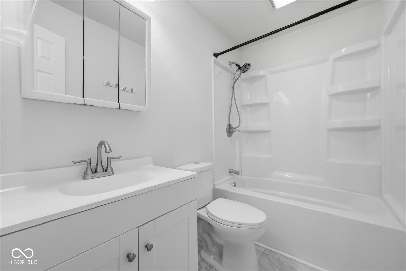 Vanity with integrated sink, tri-fold mirrored medicine cabinet, brushed nickel faucet, and a combination tub and shower