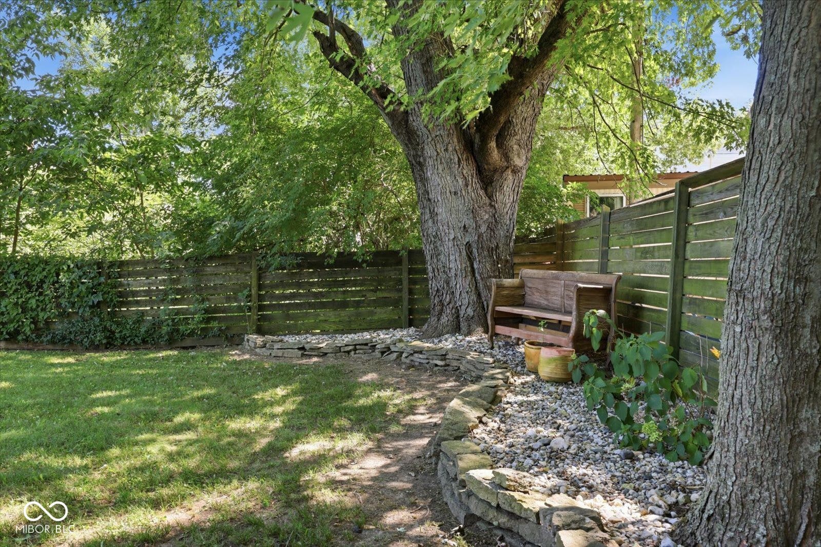 Expansive backyard featuring a manicured lawn, established trees, privacy fencing, and stone-edged landscaping