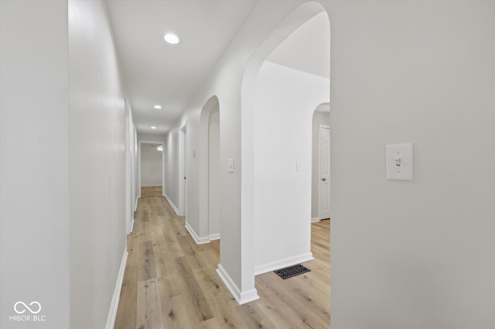 Hallway featuring wood-finish flooring, recessed lighting, arched doorways, and white trim