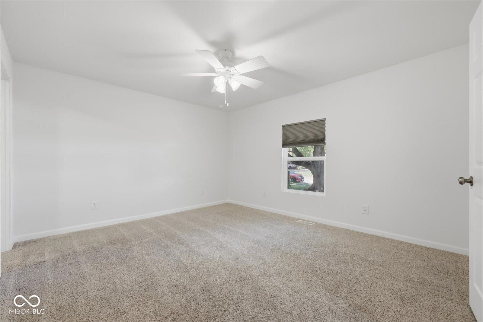 Carpeted room featuring a ceiling fan, a window with a roller shade, and white walls