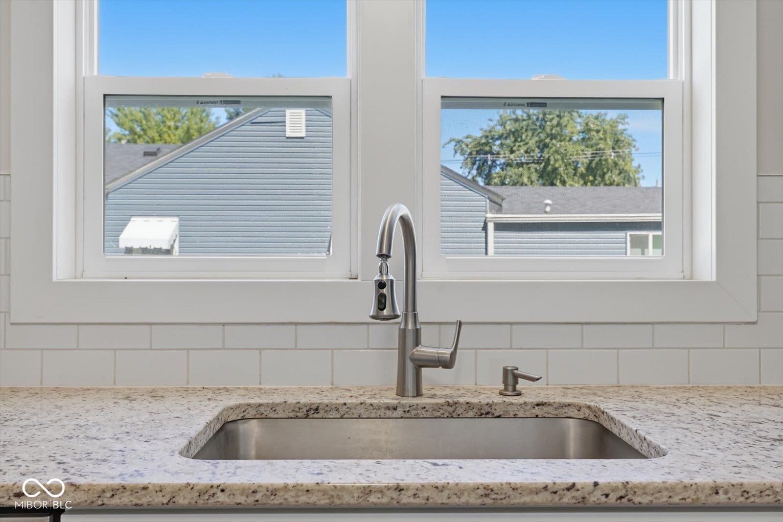 Stainless steel sink with a pull-down faucet, set into a speckled countertop, against a white subway tile backsplash