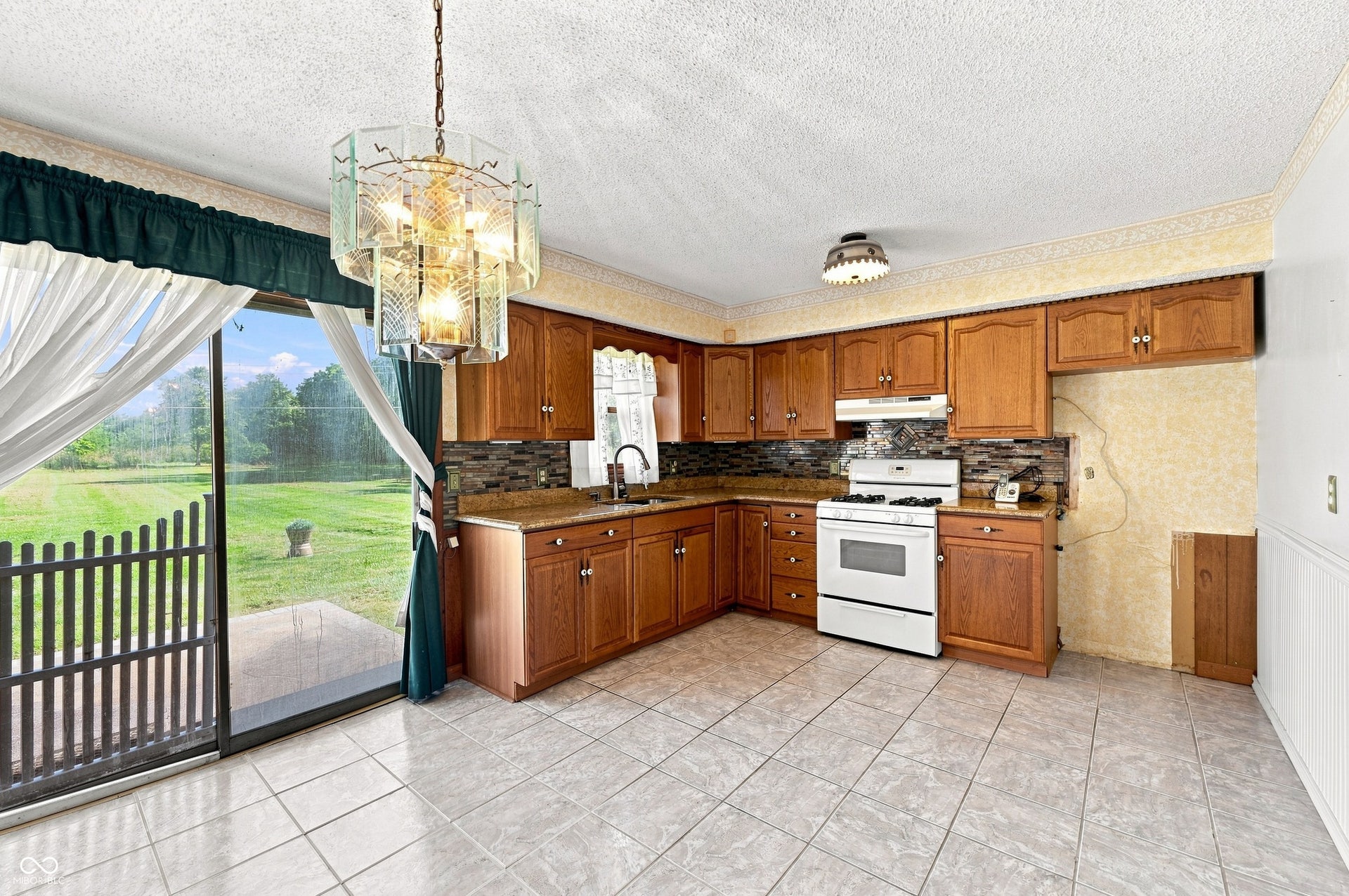 14 x 11 Kitchen with tile floors, updated cabinets, granite counter tops, glass tile splashback plus space for table and chairs with patio access.