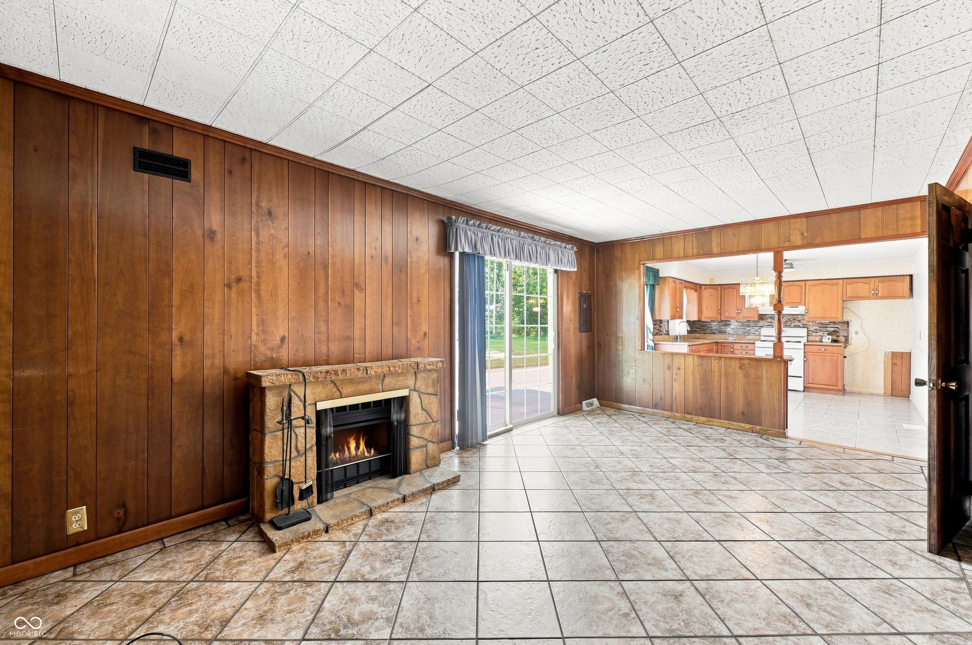 19 x 11 Family Room with tile floors, moody wood paneled walls, and propane fireplace with patio access.