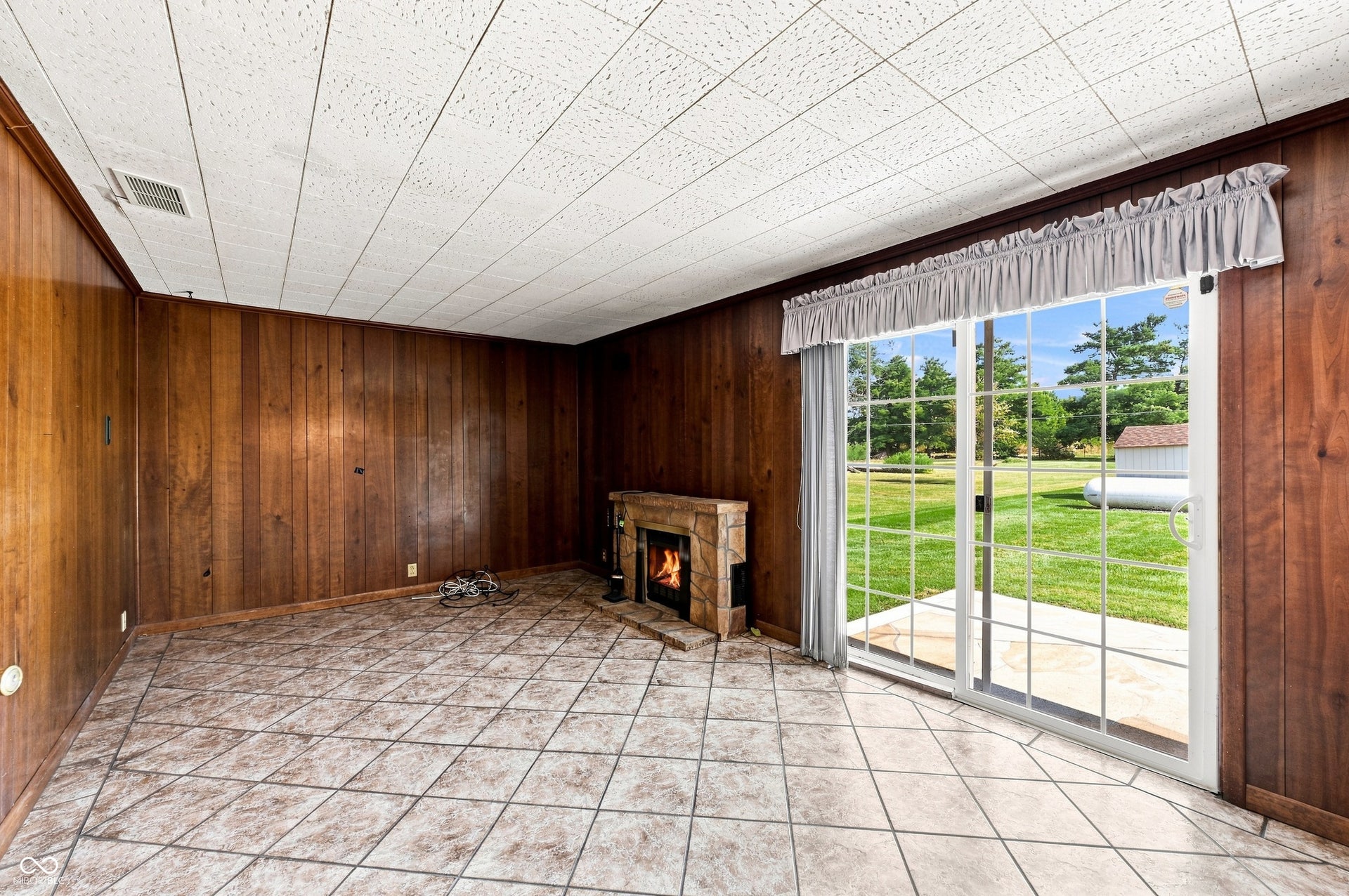 19 x 11 Family Room with tile floors, moody wood paneled walls, and propane fireplace with patio access.