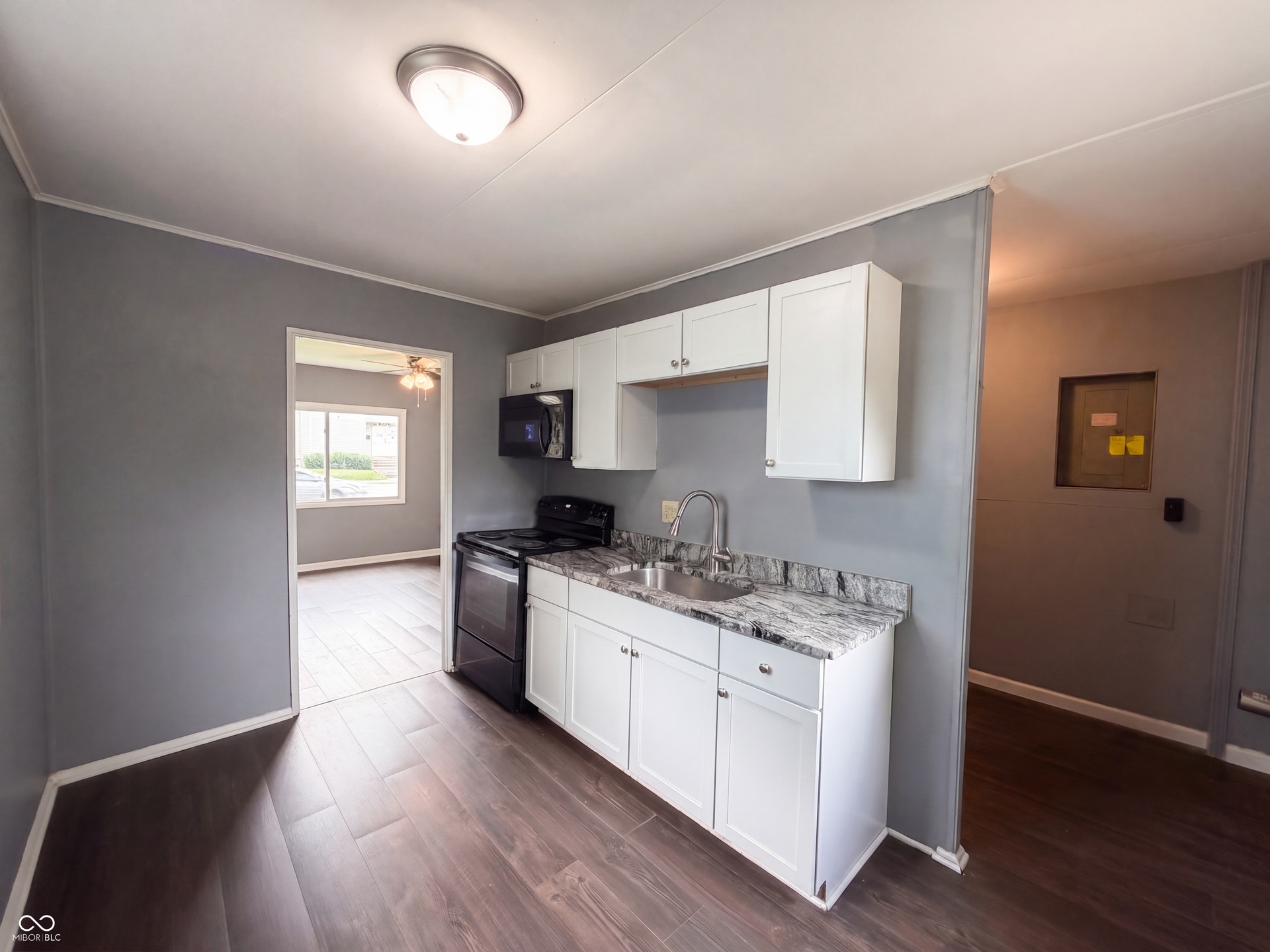 Kitchen with wood-finish flooring, white cabinetry, a stainless steel sink, and dark countertops