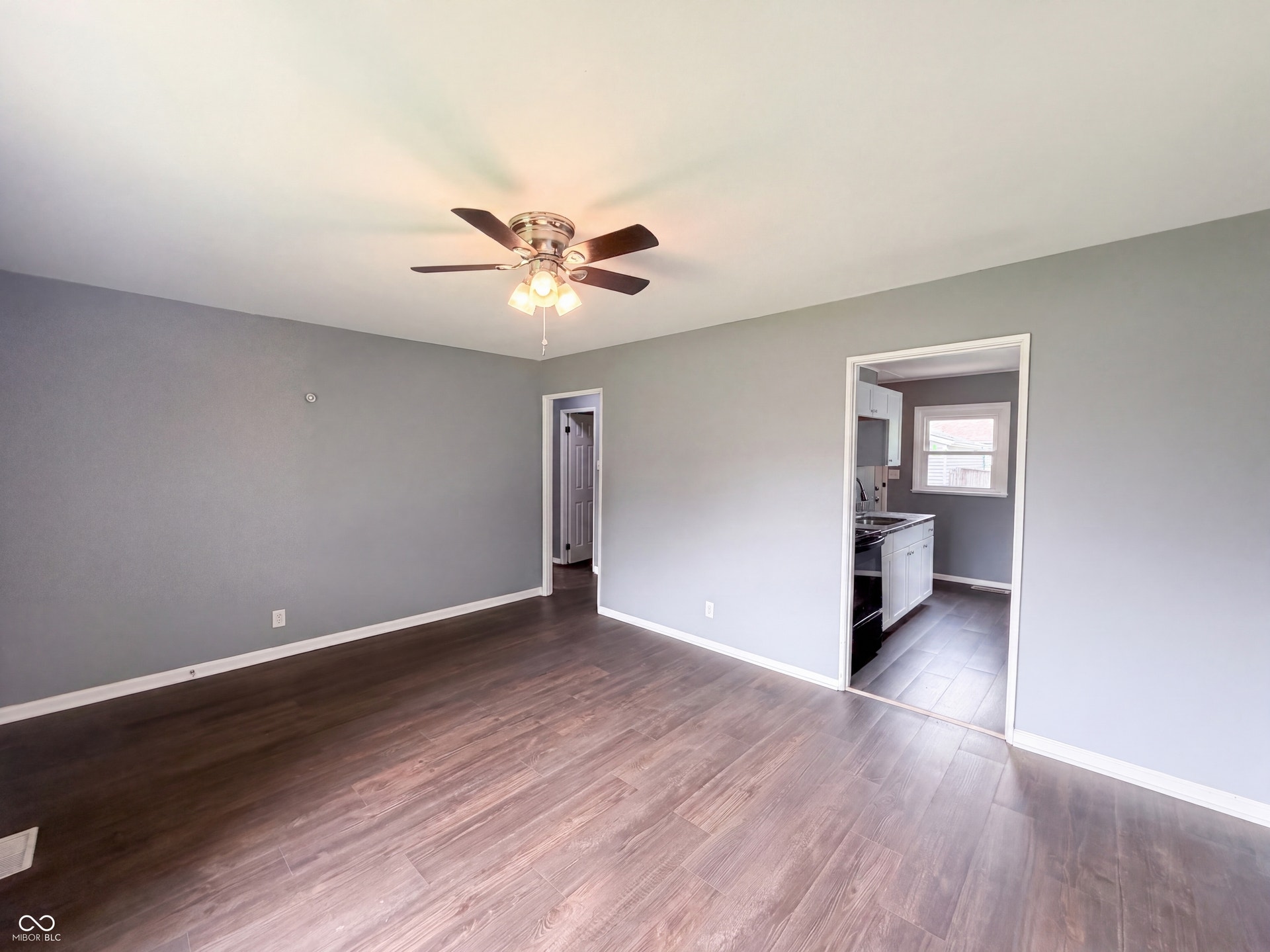 Wood-finish flooring, neutral gray walls, and a ceiling fan with integrated lighting