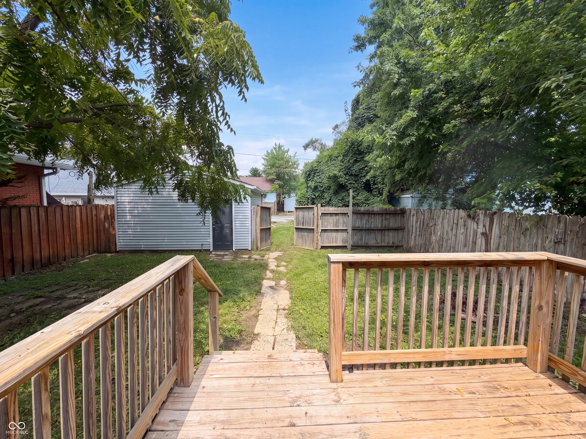 Wood-finish deck with railing, leading to a lawn area with a stone-finish pathway