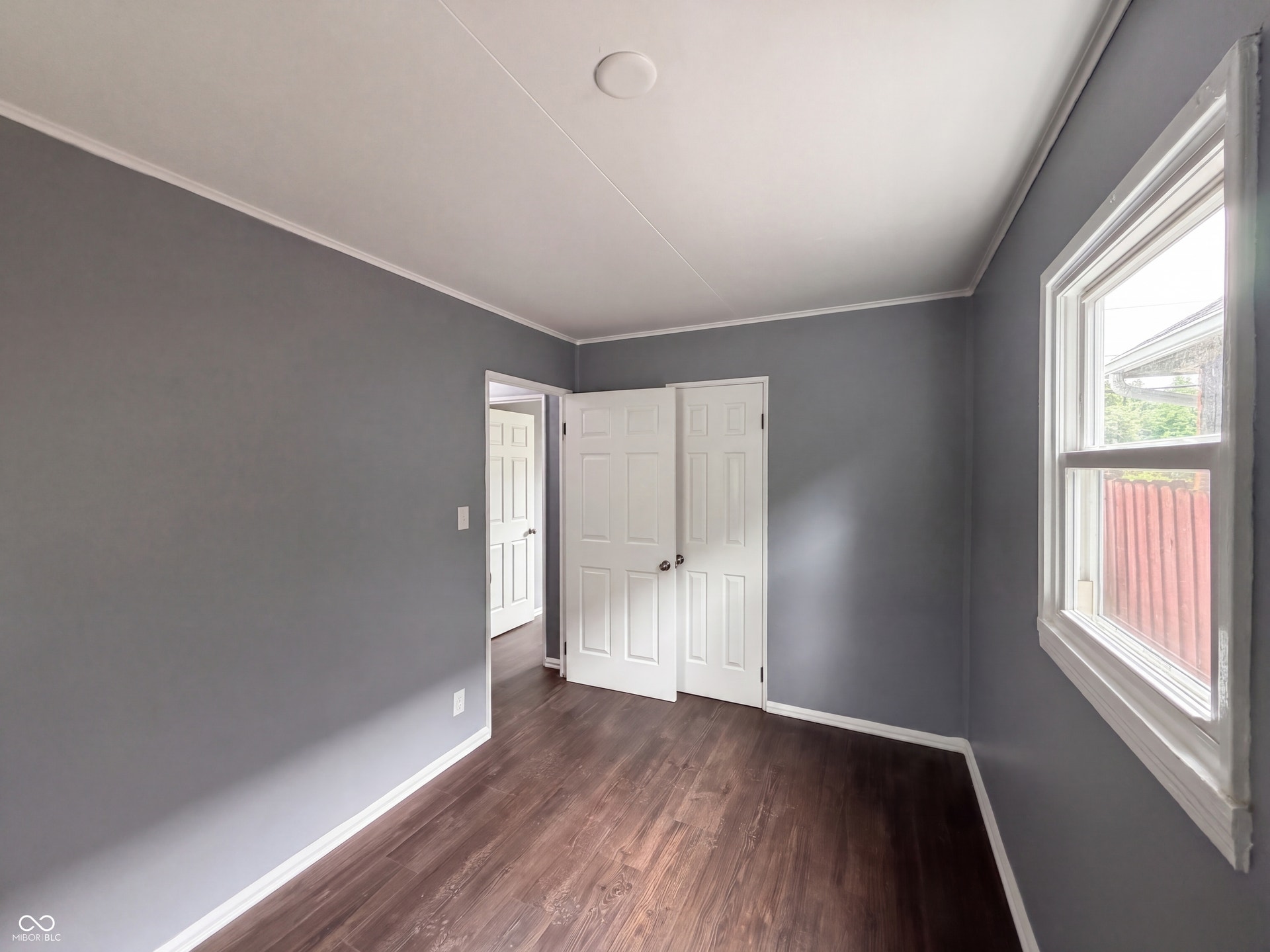 Room featuring wood-finish flooring, neutral gray walls, white trim, a double-panel door, and a window with white casing