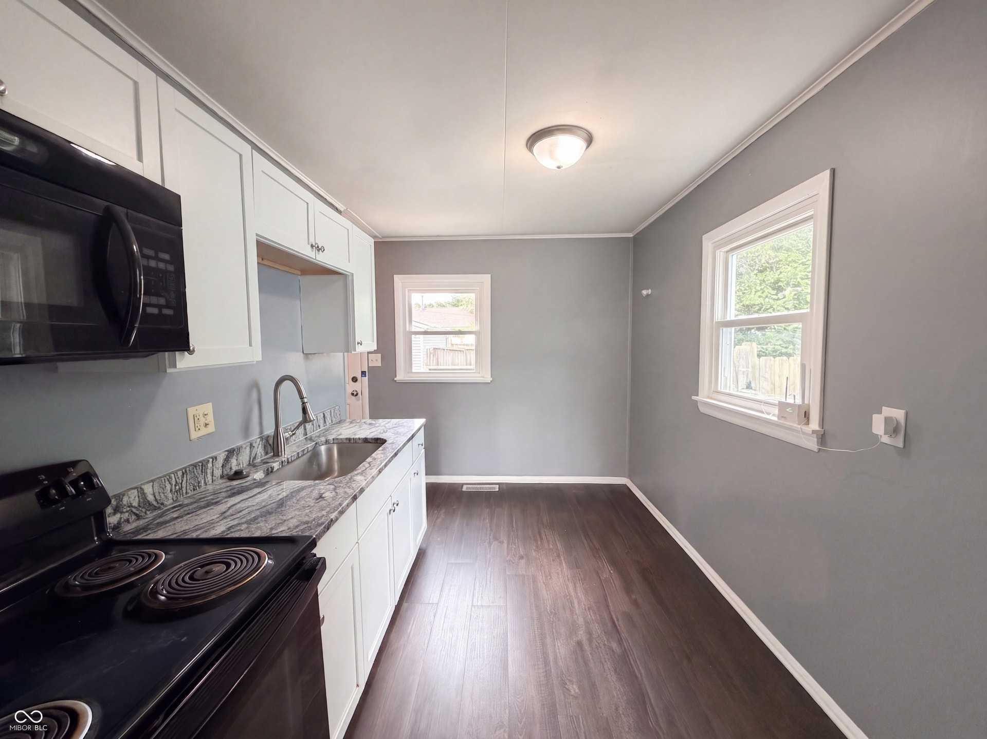 White shaker-style cabinetry with crown molding, integrated microwave, black electric range, stainless steel sink, and wood-finish flooring