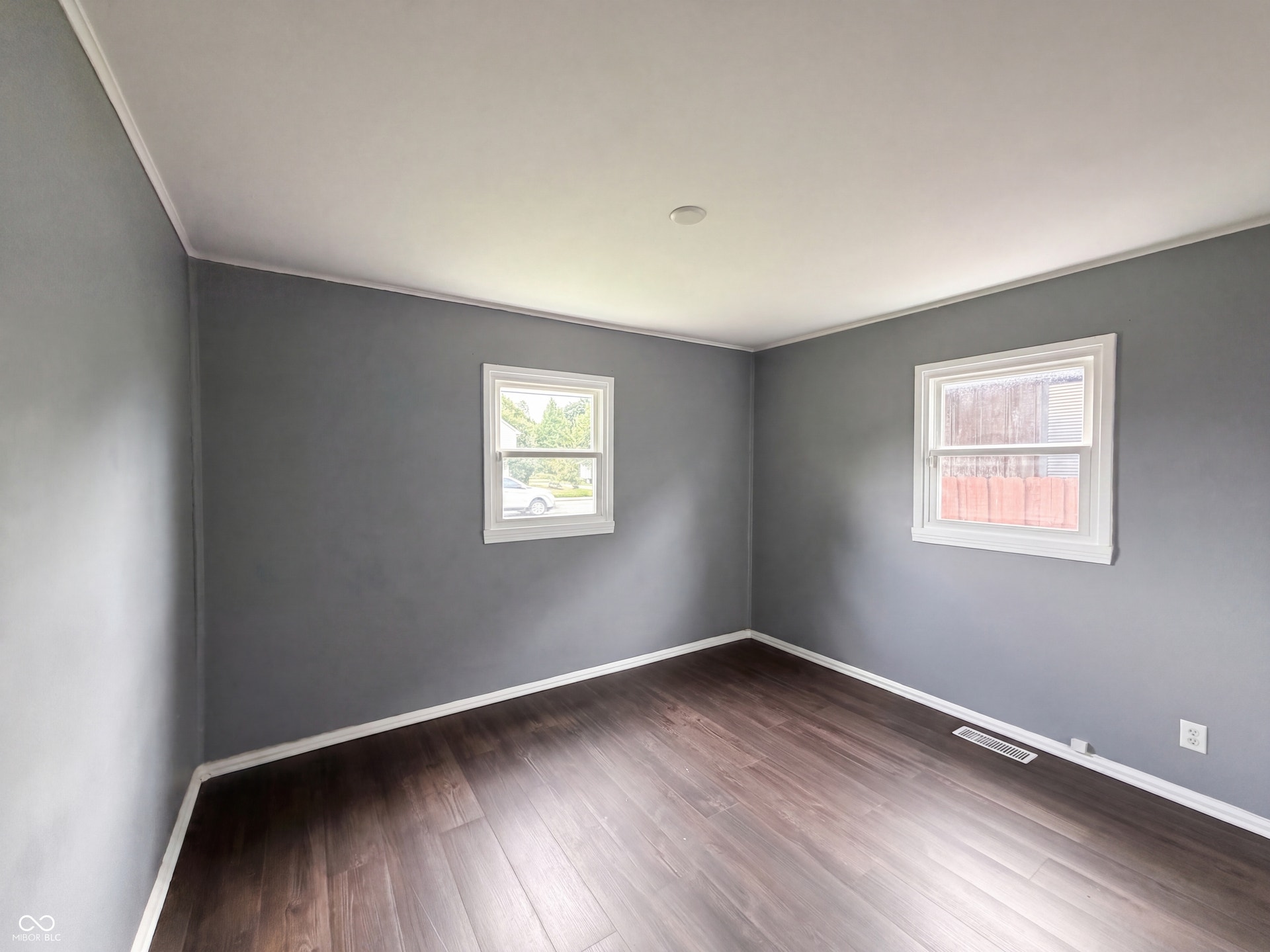 Wood-finish flooring, two windows with white trim, gray wall paint, white ceiling, and a recessed ceiling light