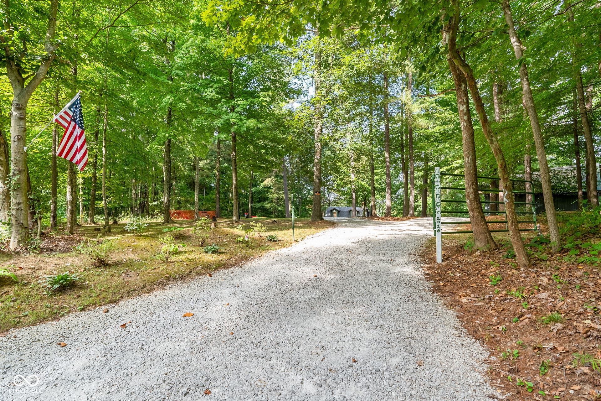 Gated gravel driveway surrounded by mature trees and natural landscaping