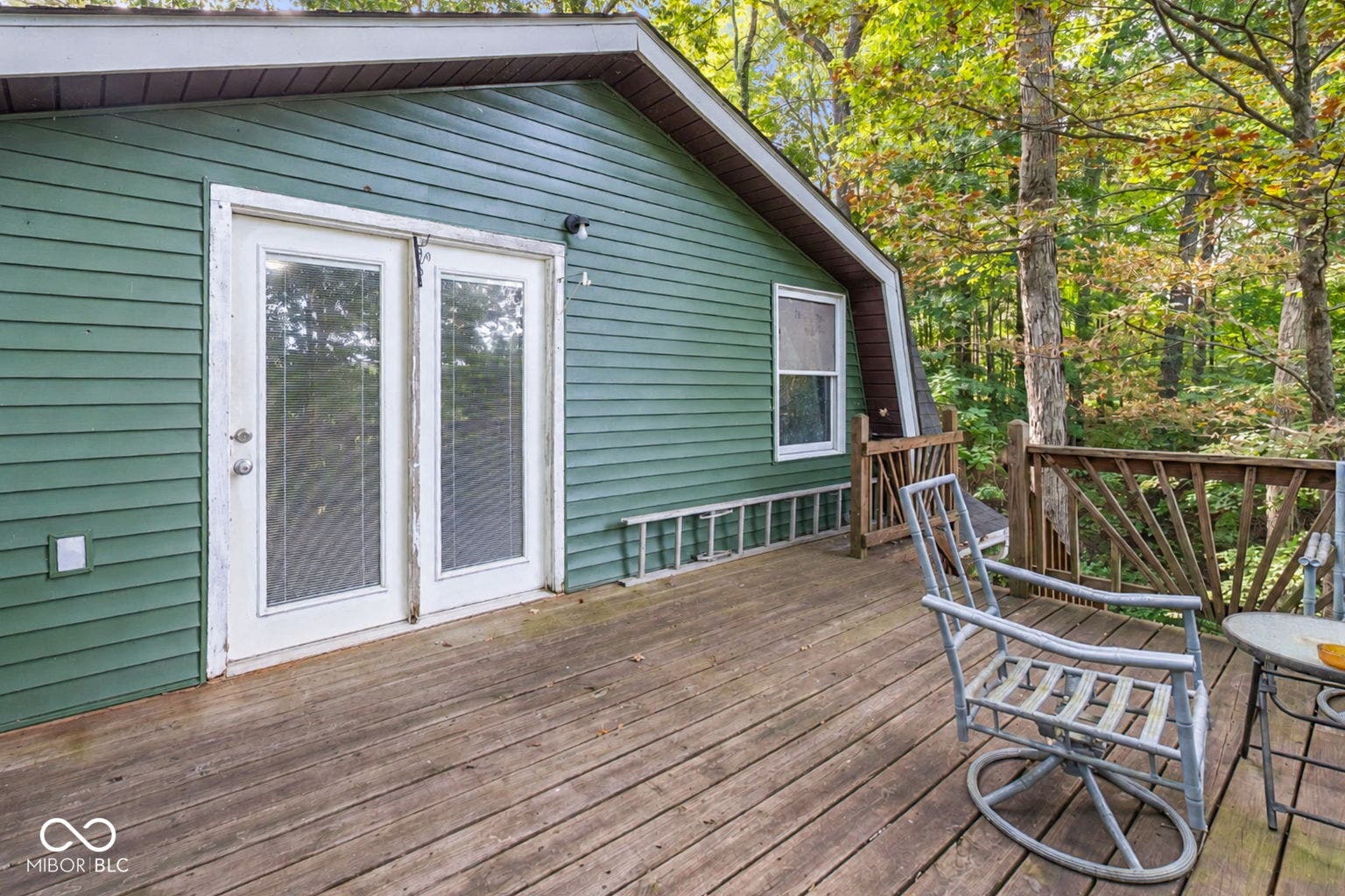 Wood-finish deck with a wood railing, double glass-panel doors, and a forest backdrop