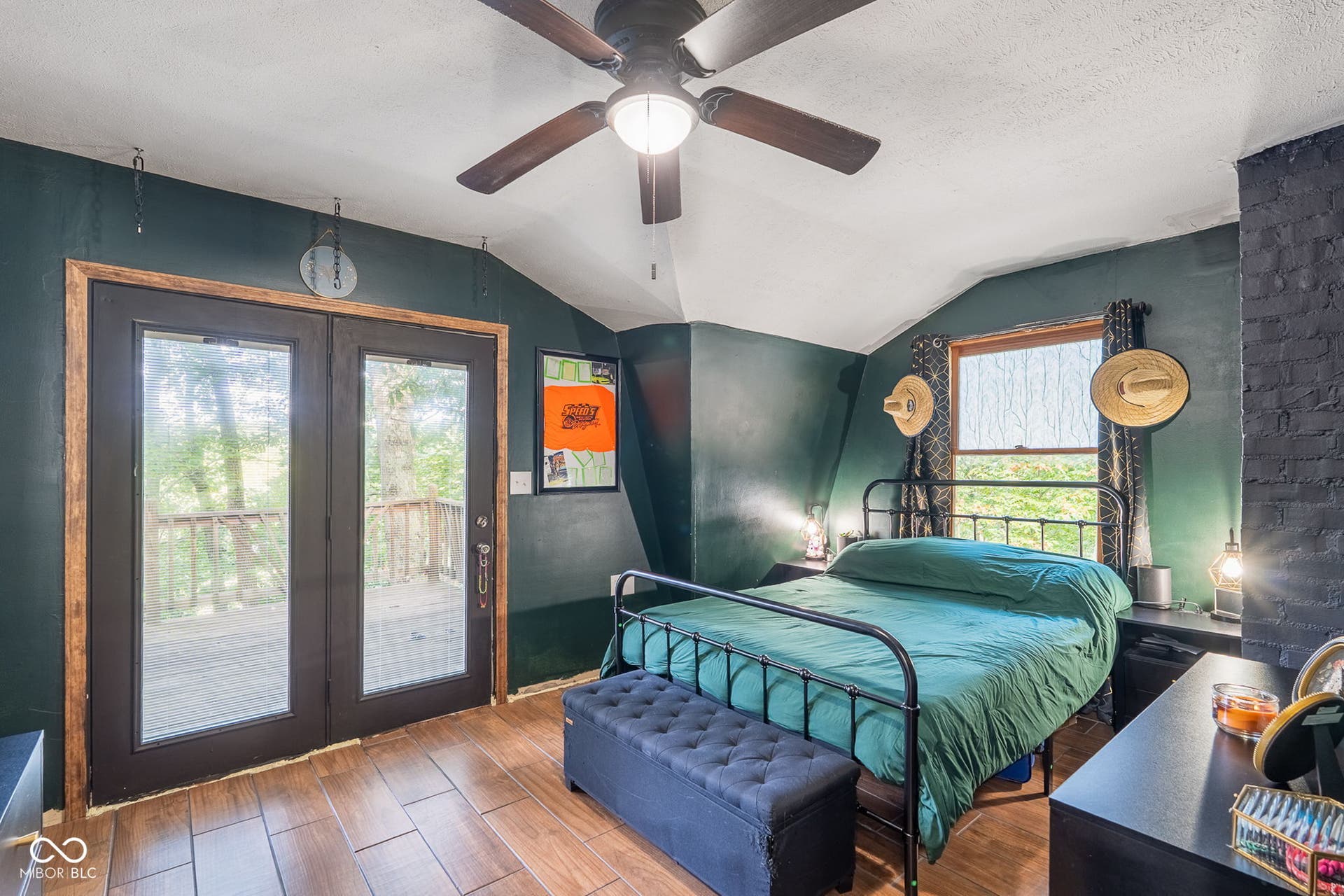Wood-finish flooring, ceiling fan, dark painted brick accent wall, and glass-paneled double doors opening to an exterior deck