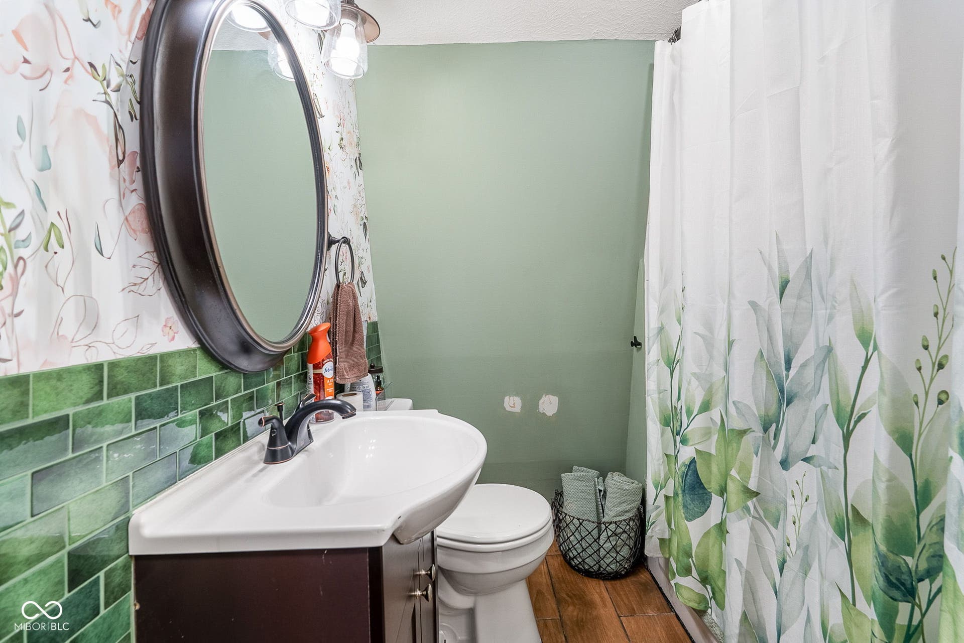 Partial green subway tile wainscoting and a wall-mounted oval mirror