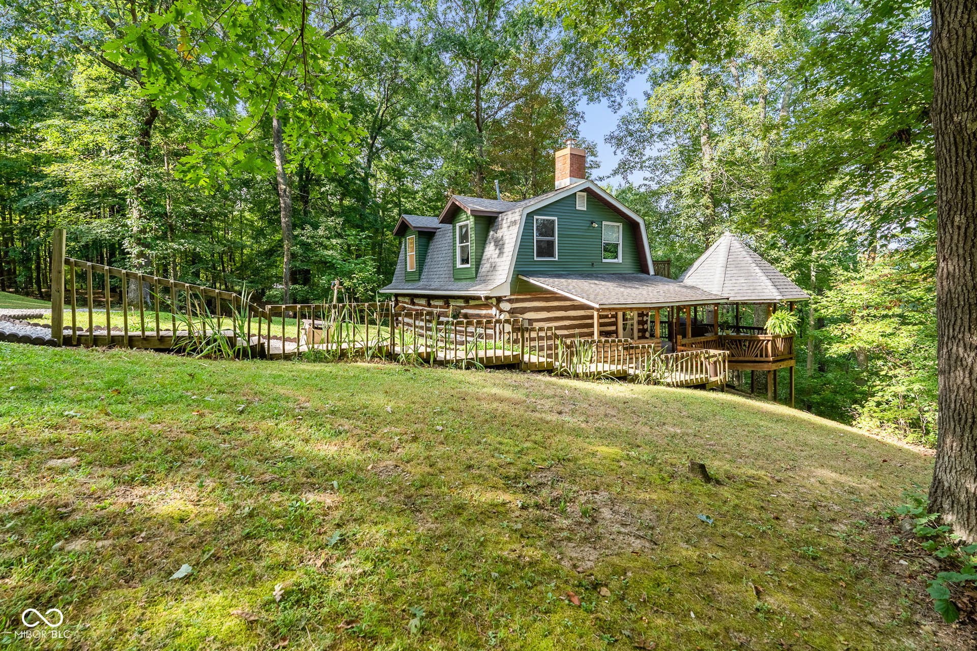Log cabin exterior with a gambrel roofline, a wraparound porch, and a detached gazebo