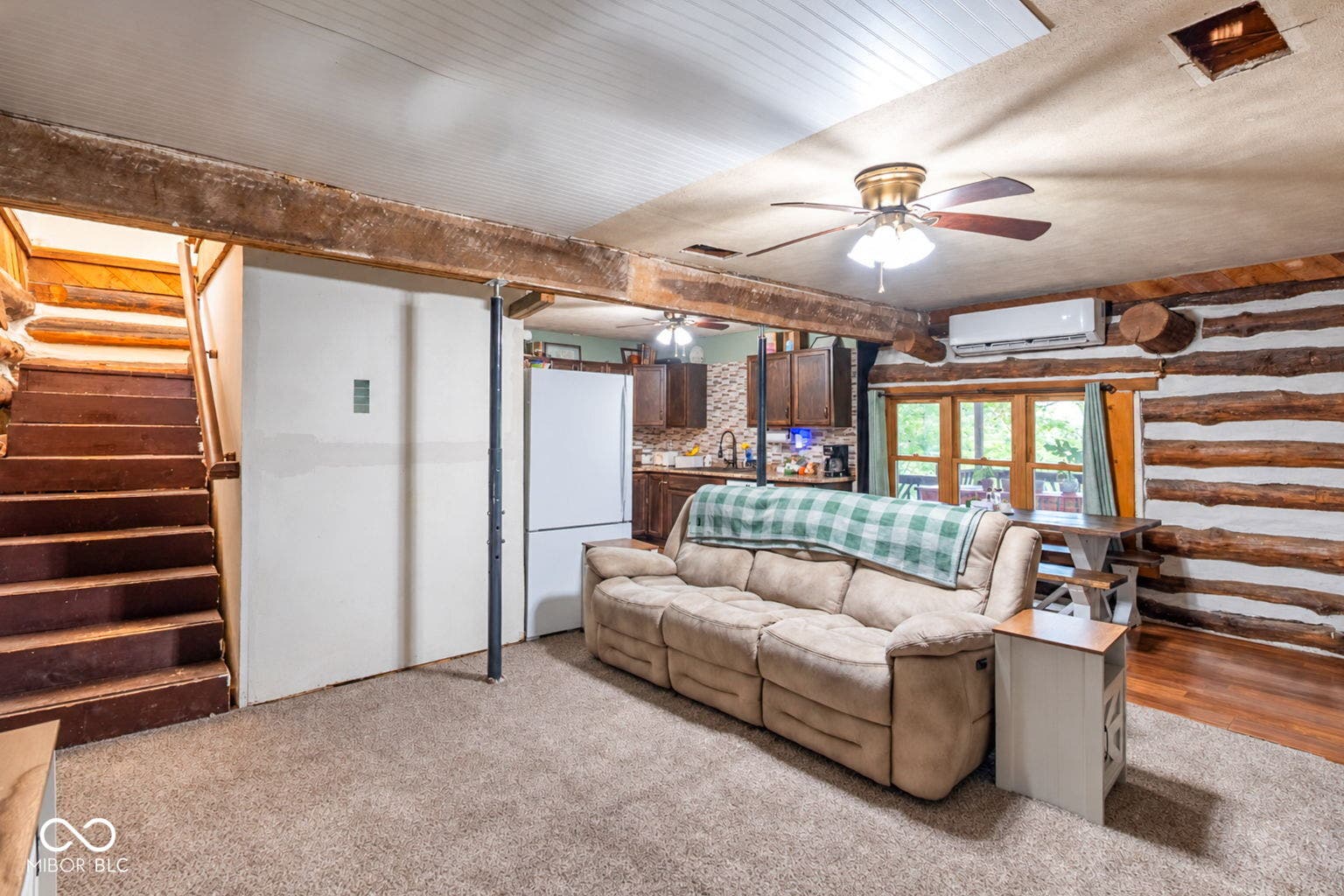 Wood-finish staircase with log banister, wood-beam ceiling, exposed log wall, wood-frame windows, and ceiling fan