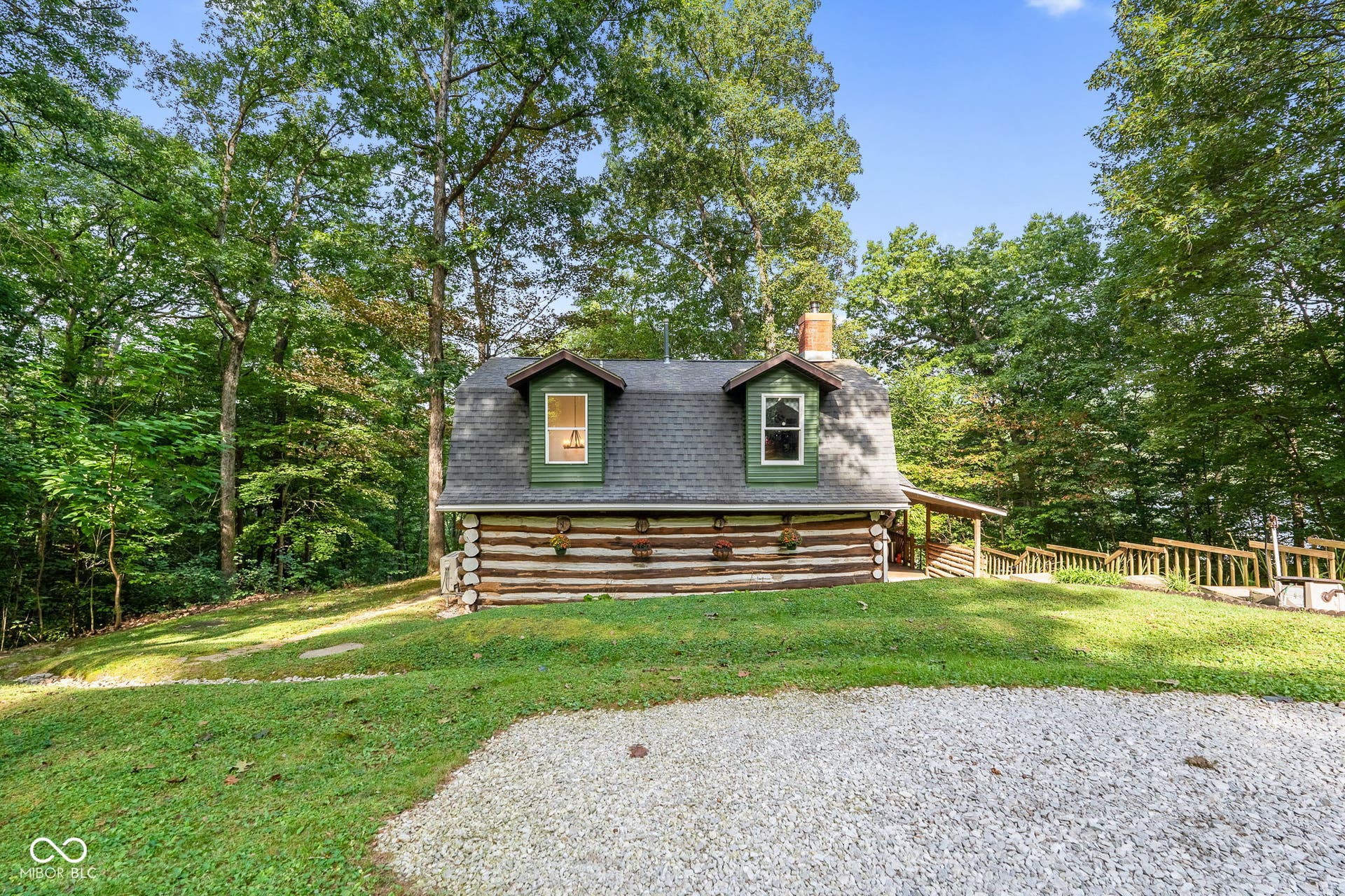 Log cabin exterior with a gambrel roof, two dormer windows, and a brick chimney