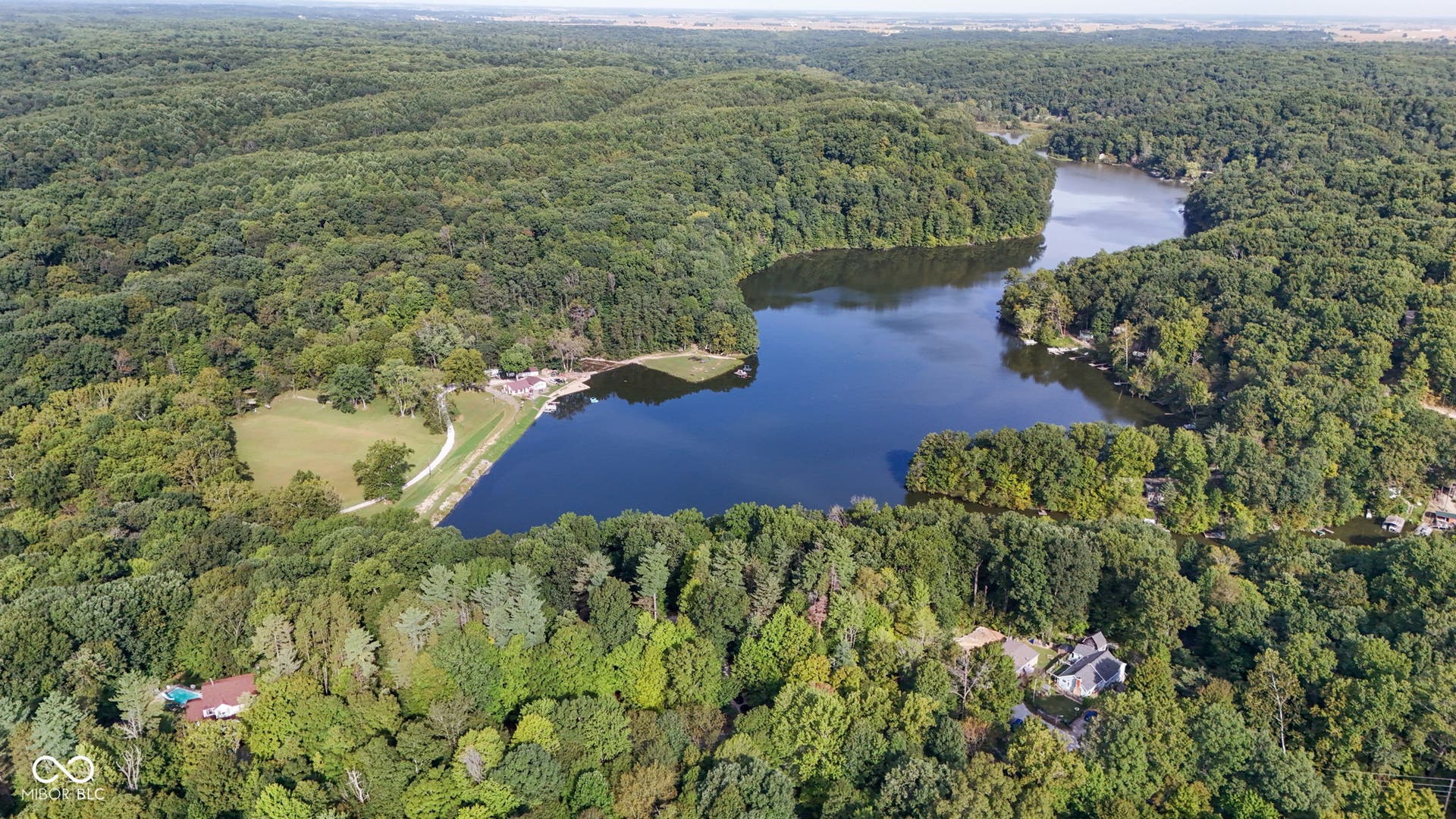 Expansive wooded property featuring a lake, shoreline, and scattered residential structures