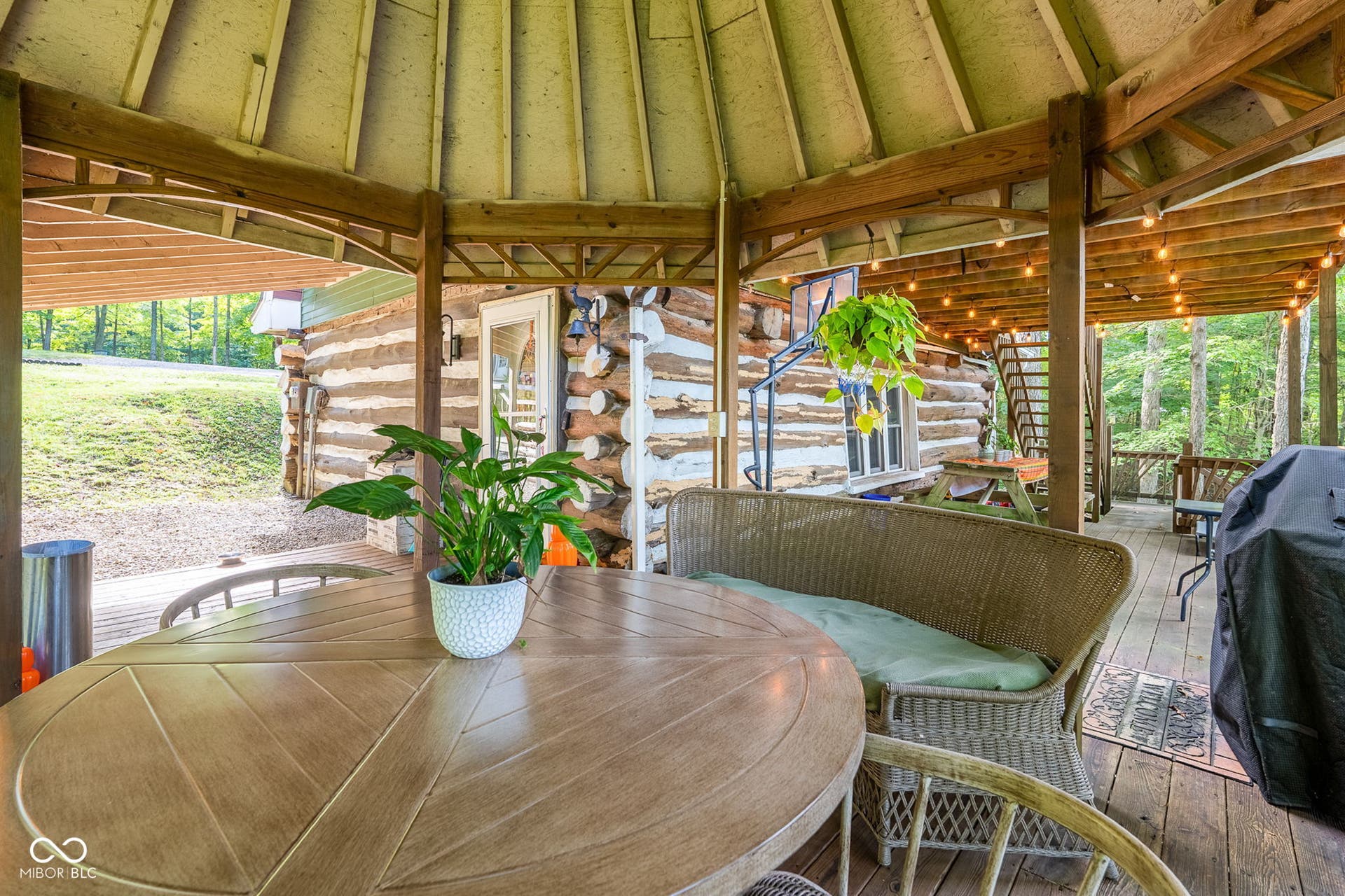 Expansive covered deck featuring a natural wood ceiling, wood plank flooring, string lighting, and log cabin exterior
