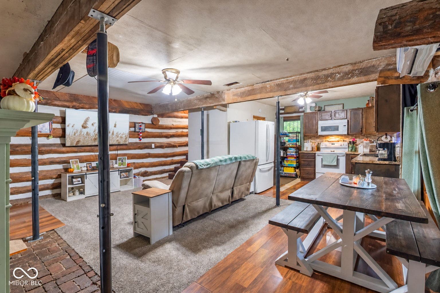 Exposed log wall paneling, wood-finish flooring, ceiling fan, kitchen with wood cabinetry, and dining area with built-in bench seating