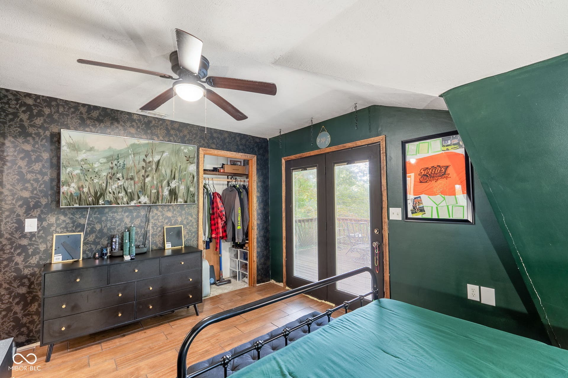 Wood-finish flooring, ceiling fan with integrated lighting, double-door access to an outdoor deck, and built-in closet with shelving